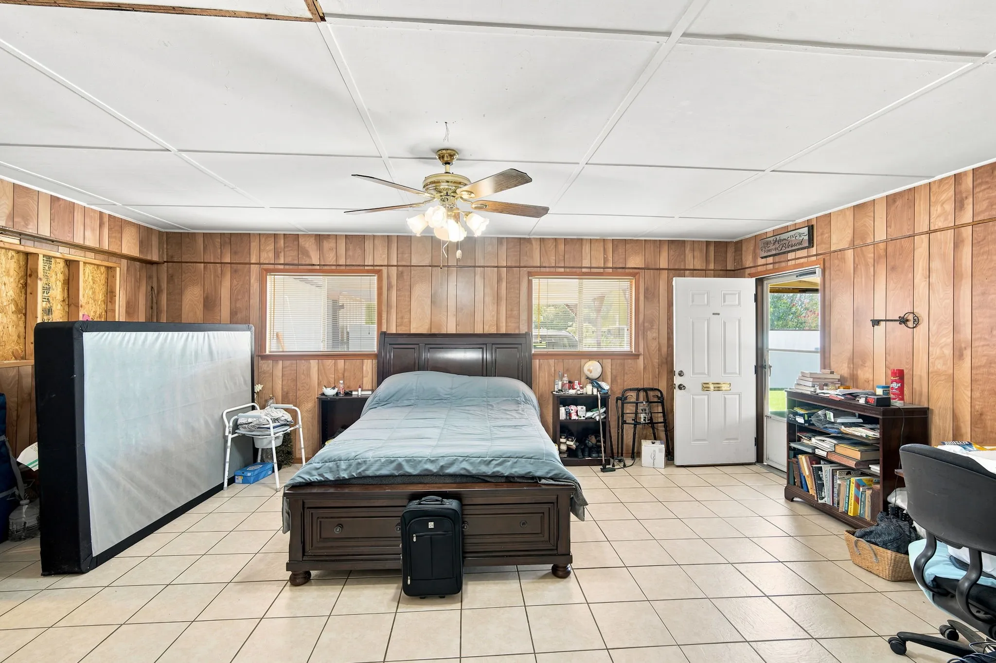 Spacious room featuring wood paneling, light-colored tile flooring, and a ceiling fan with integrated lighting