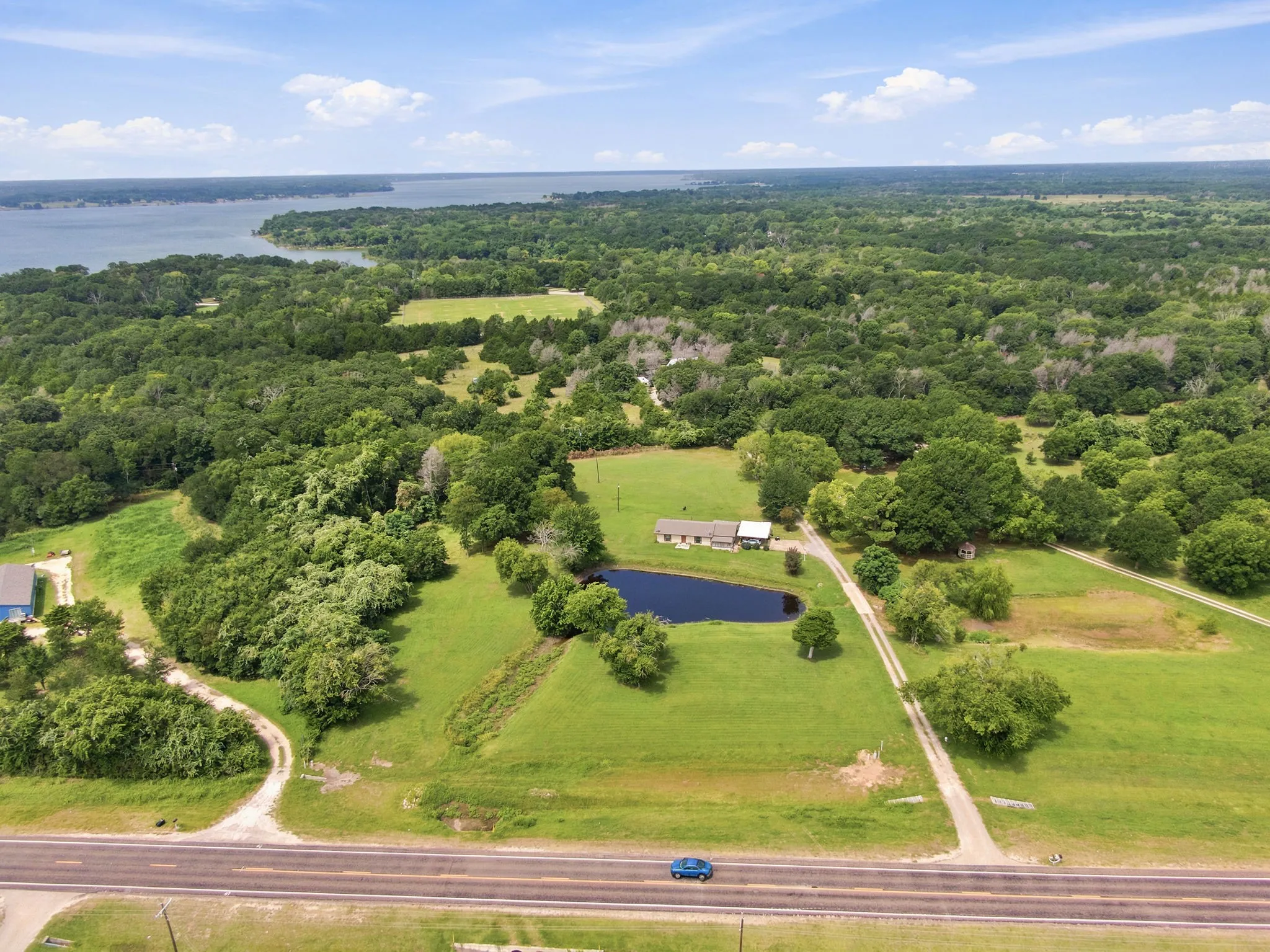 Expansive property featuring a single-story residence, private pond, and mature trees, bordered by a main road and surrounded by abundant greenery