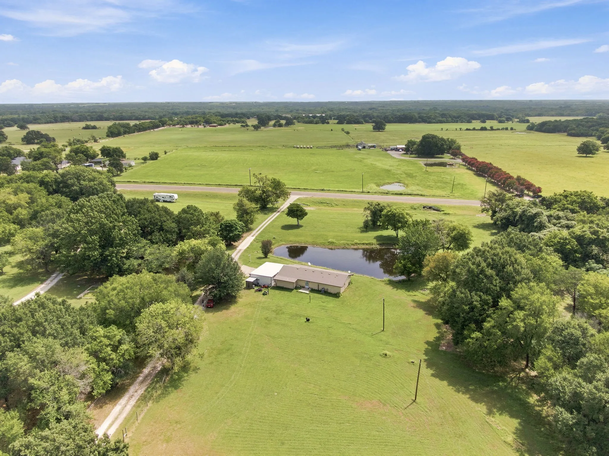 Expansive green acreage featuring a single-story home, a private pond, mature trees, and a gravel driveway