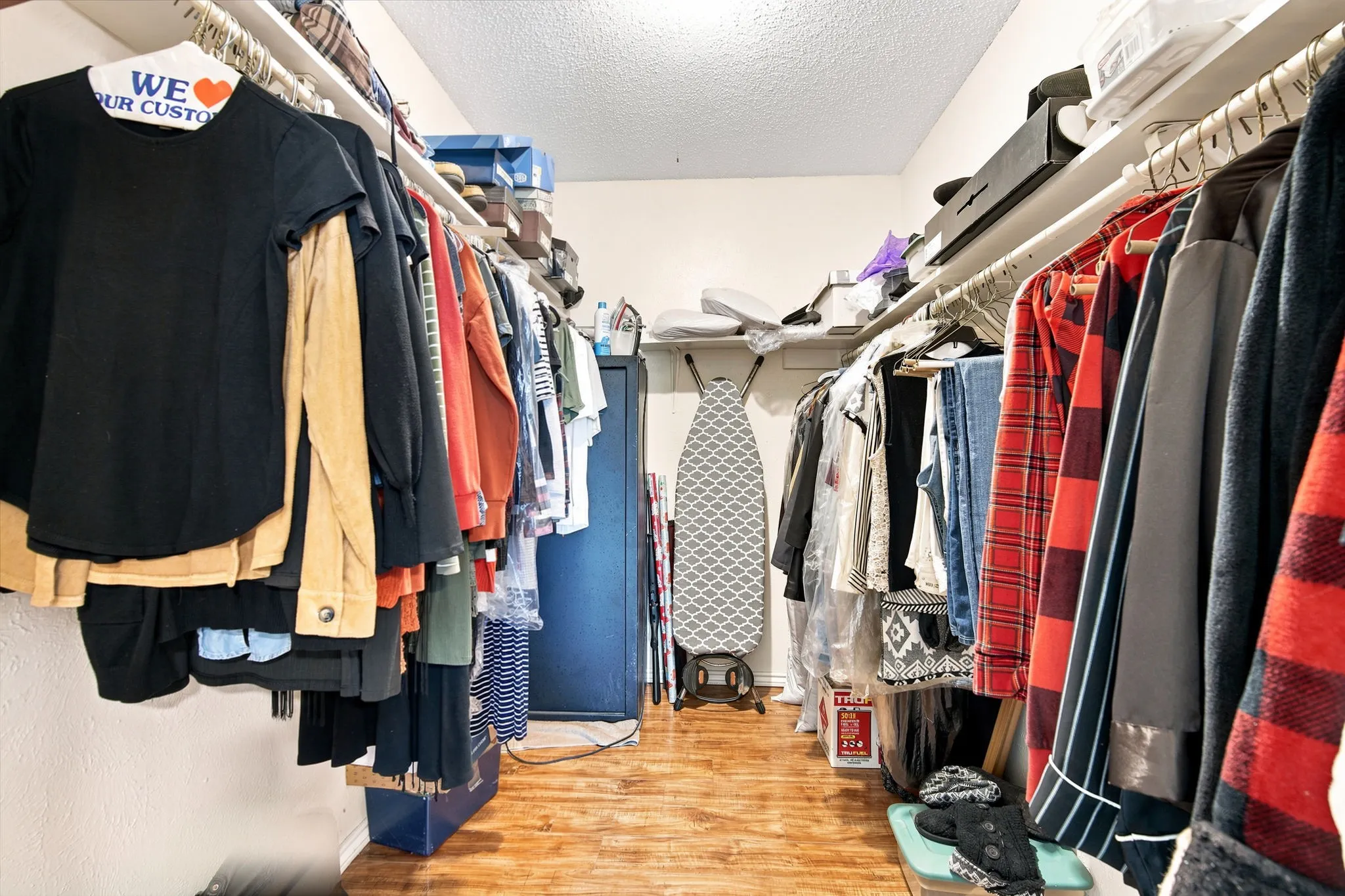 Walk-in closet featuring wood-finish flooring, white walls, and extensive shelving and hanging rods on both sides