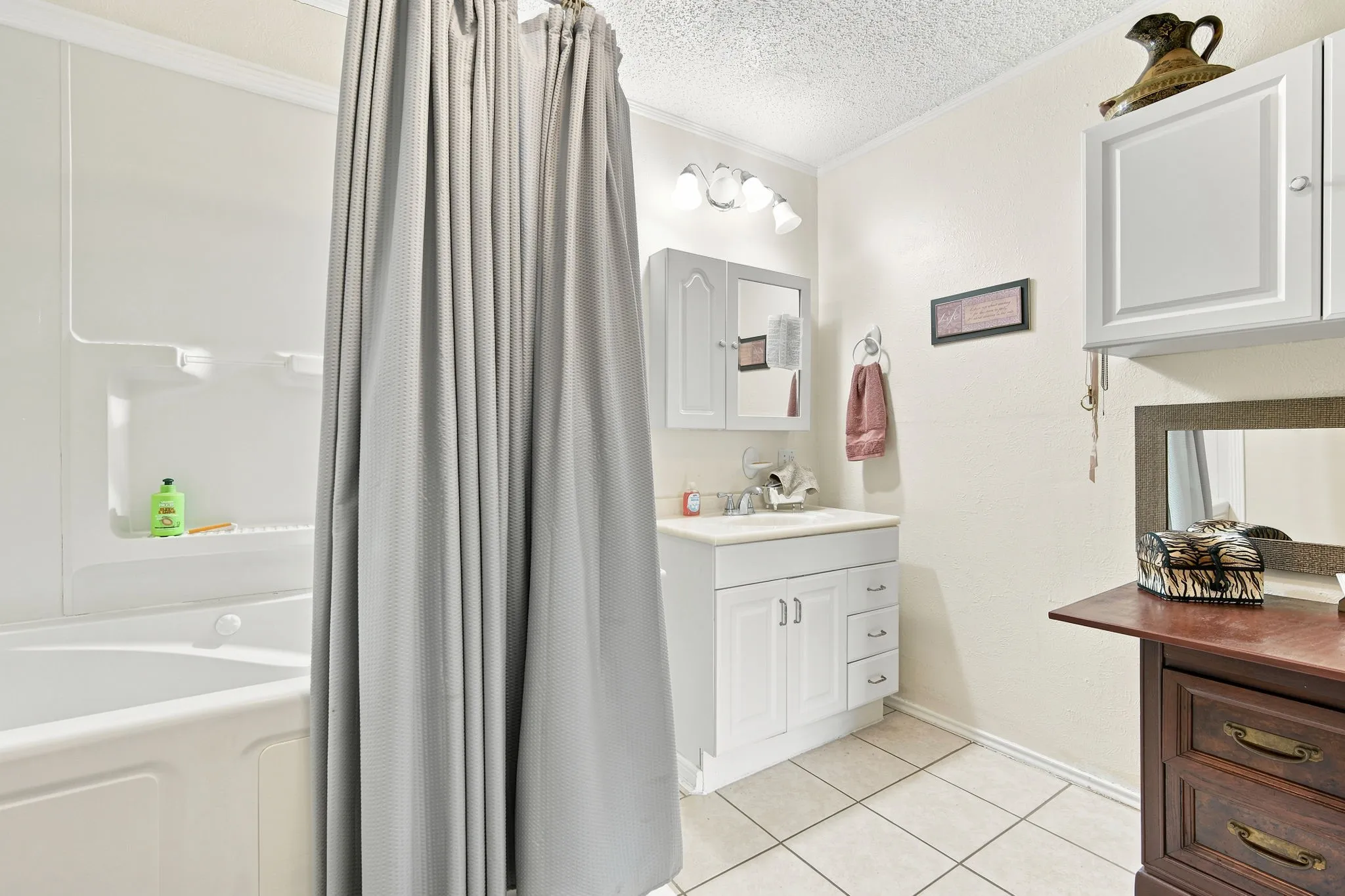 Bathroom featuring a white bathtub with an integrated shower, a white vanity with an undermount sink, and light-toned tile flooring