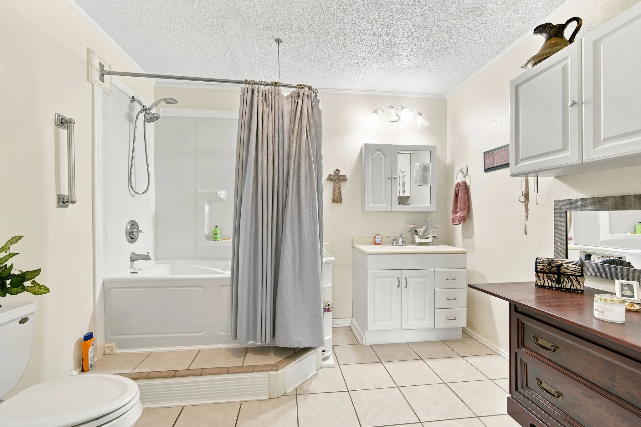 Bathroom featuring a white tub and shower combination with a curved shower rod, a white single vanity with integrated sink, and white wall-mounted cabinetry