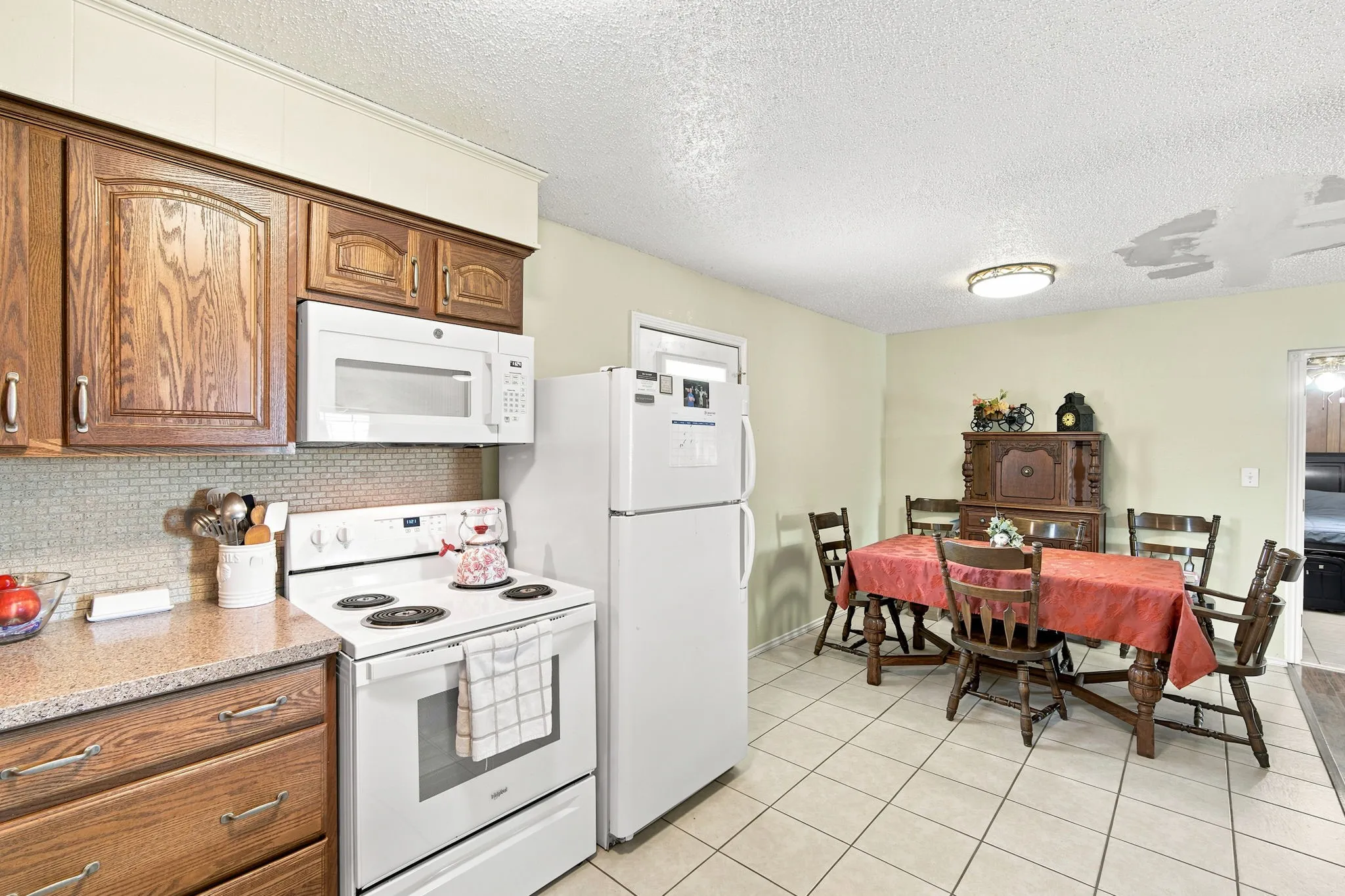Kitchen and dining area featuring wood cabinetry, white appliances, a tile backsplash, and tile flooring