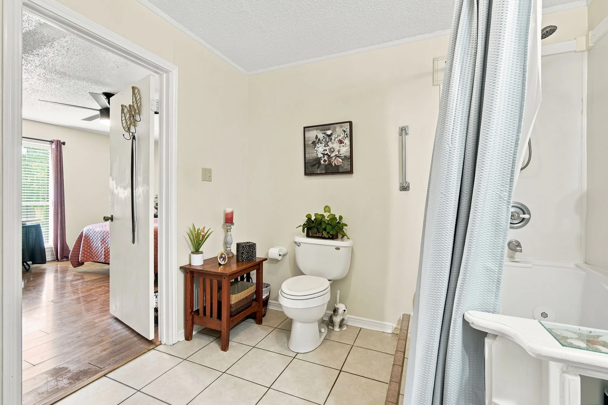 Bathroom featuring white tiled flooring, a built-in tub with shower, and a white toilet