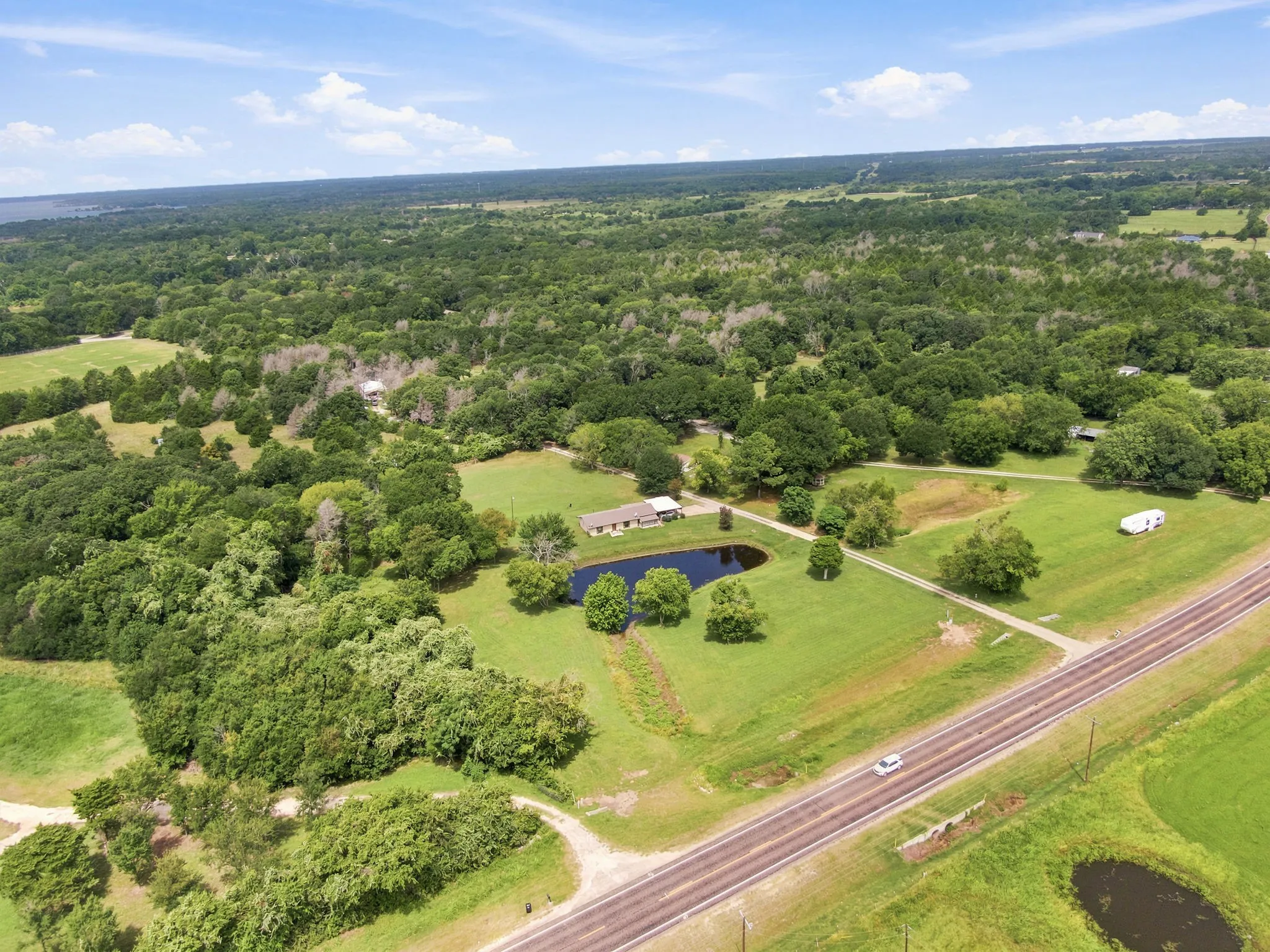 Expansive rural property featuring a private pond, open green spaces, mature trees, and direct road frontage