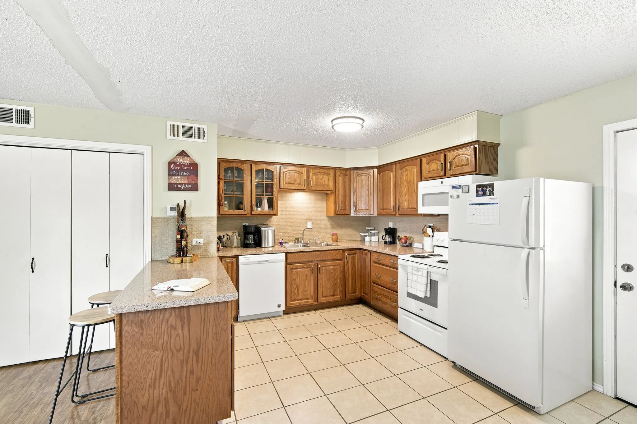 Kitchen featuring light wood cabinetry, white appliances, and a breakfast bar with a stone-finish countertop