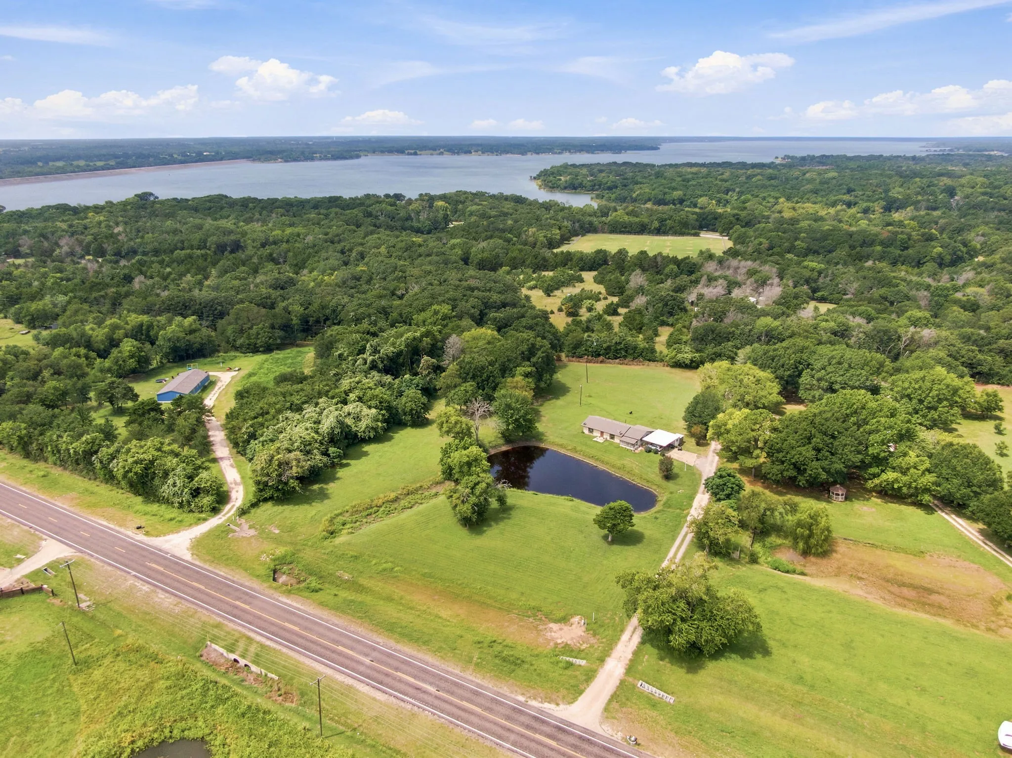 Expansive property featuring a private pond, a single-story residence, and a separate blue-roofed outbuilding