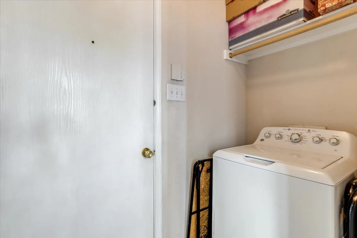 Dedicated laundry area featuring a top-loading appliance, overhead shelving, and a hanging rod