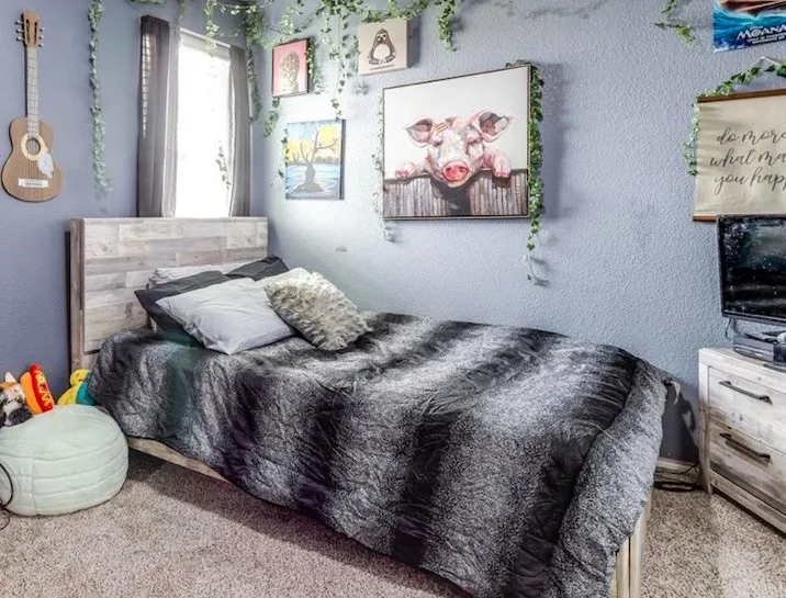Carpeted room featuring a window with dark drapes, a wood-finish headboard, textured light blue walls, and a matching wood-finish nightstand with dark hardware