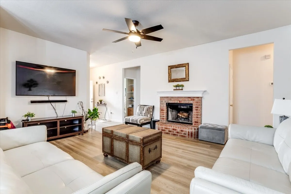 Living room featuring luxury vinyl plank flooring, a brick fireplace with mantel, and a ceiling fan with integrated lighting