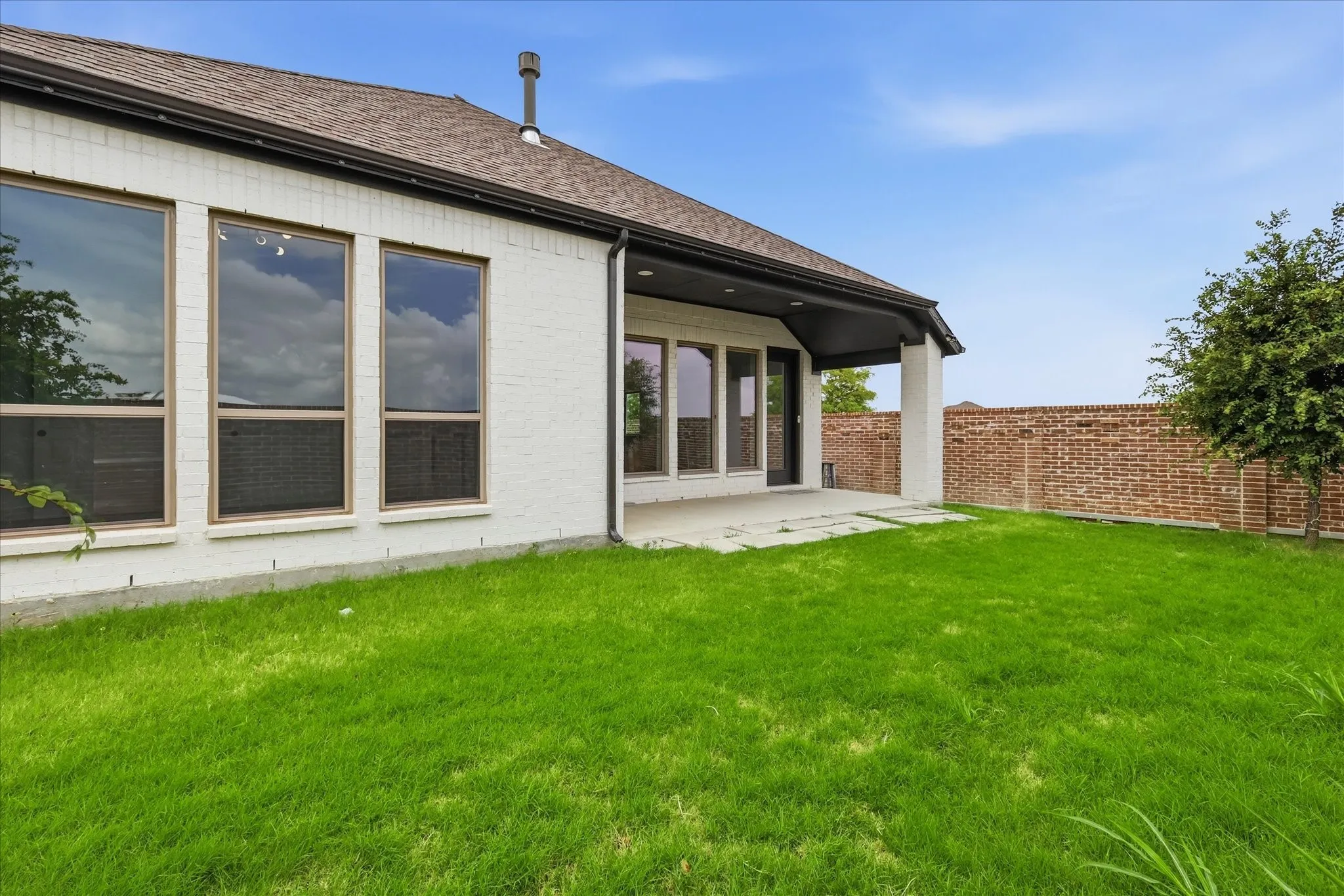 Spacious backyard featuring a covered patio with concrete flooring, a lush green lawn, and a privacy brick fence