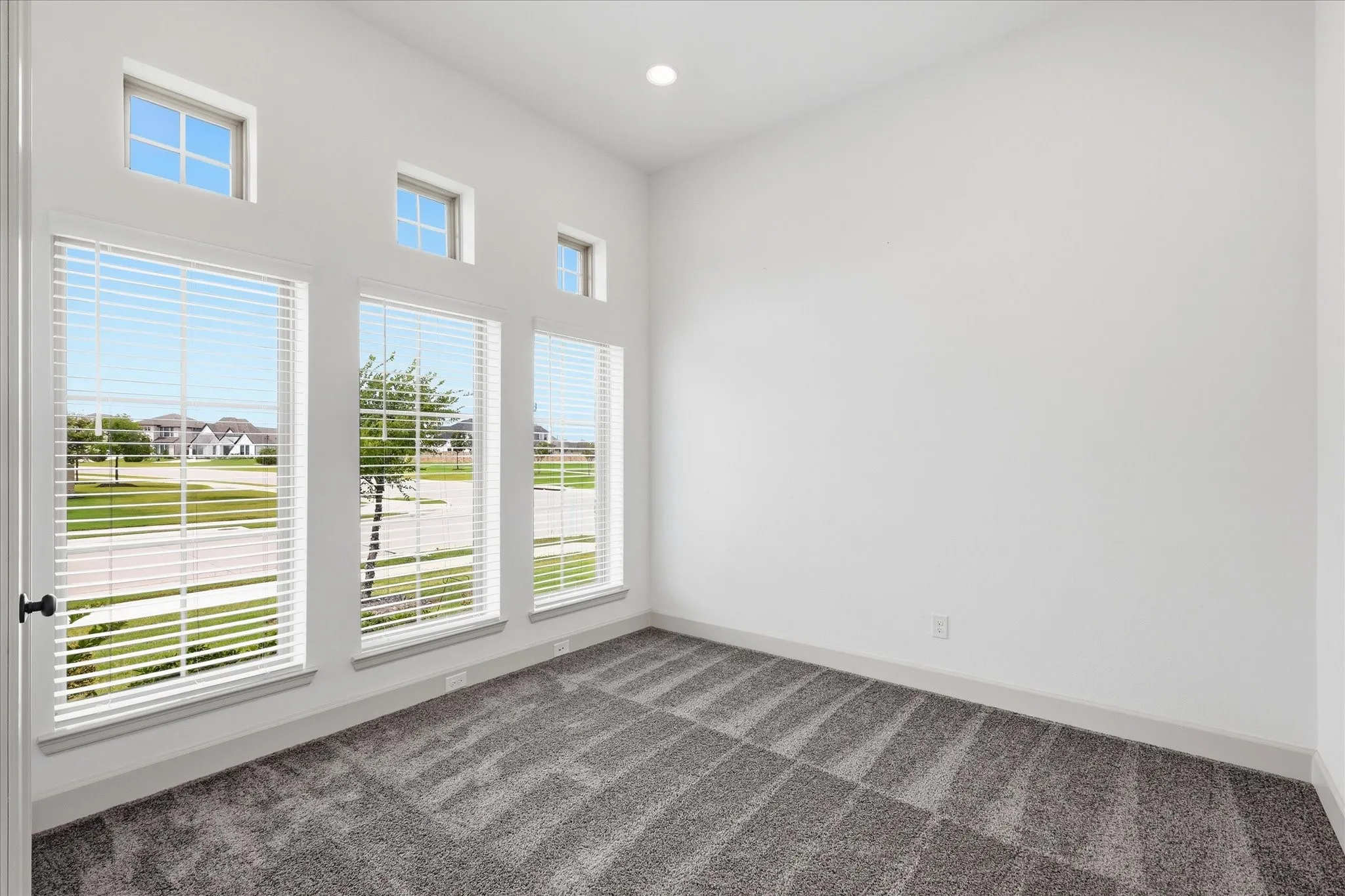 Room with vaulted ceiling, featuring multiple large windows with white blinds