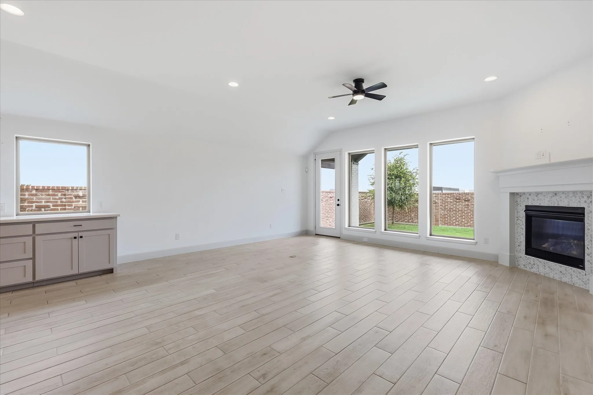 Spacious room featuring light wood-finish flooring, a fireplace with a textured tile surround and white mantle, and multiple large windows