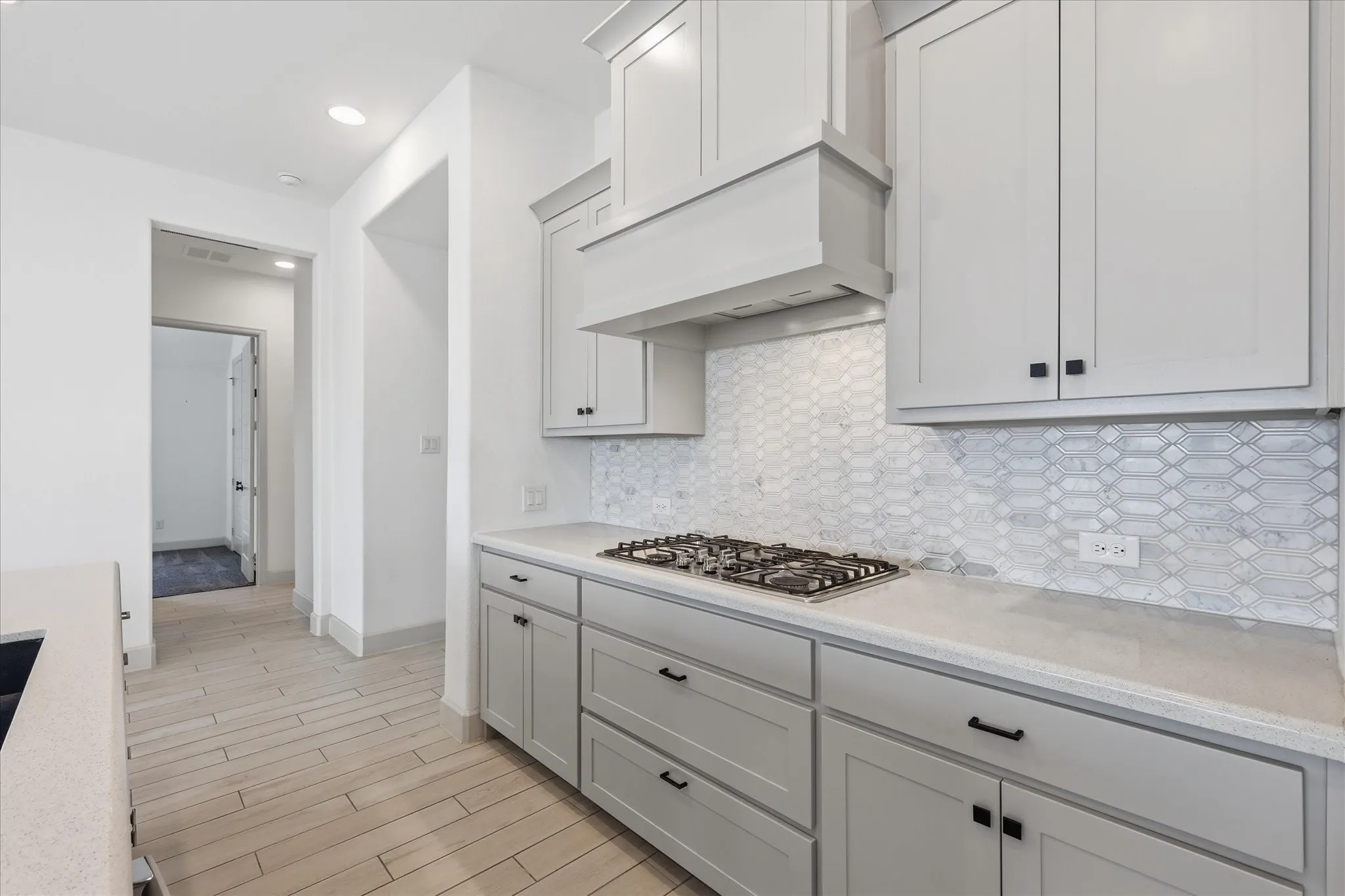Modern kitchen featuring light gray cabinetry, a built-in gas cooktop, and a decorative range hood