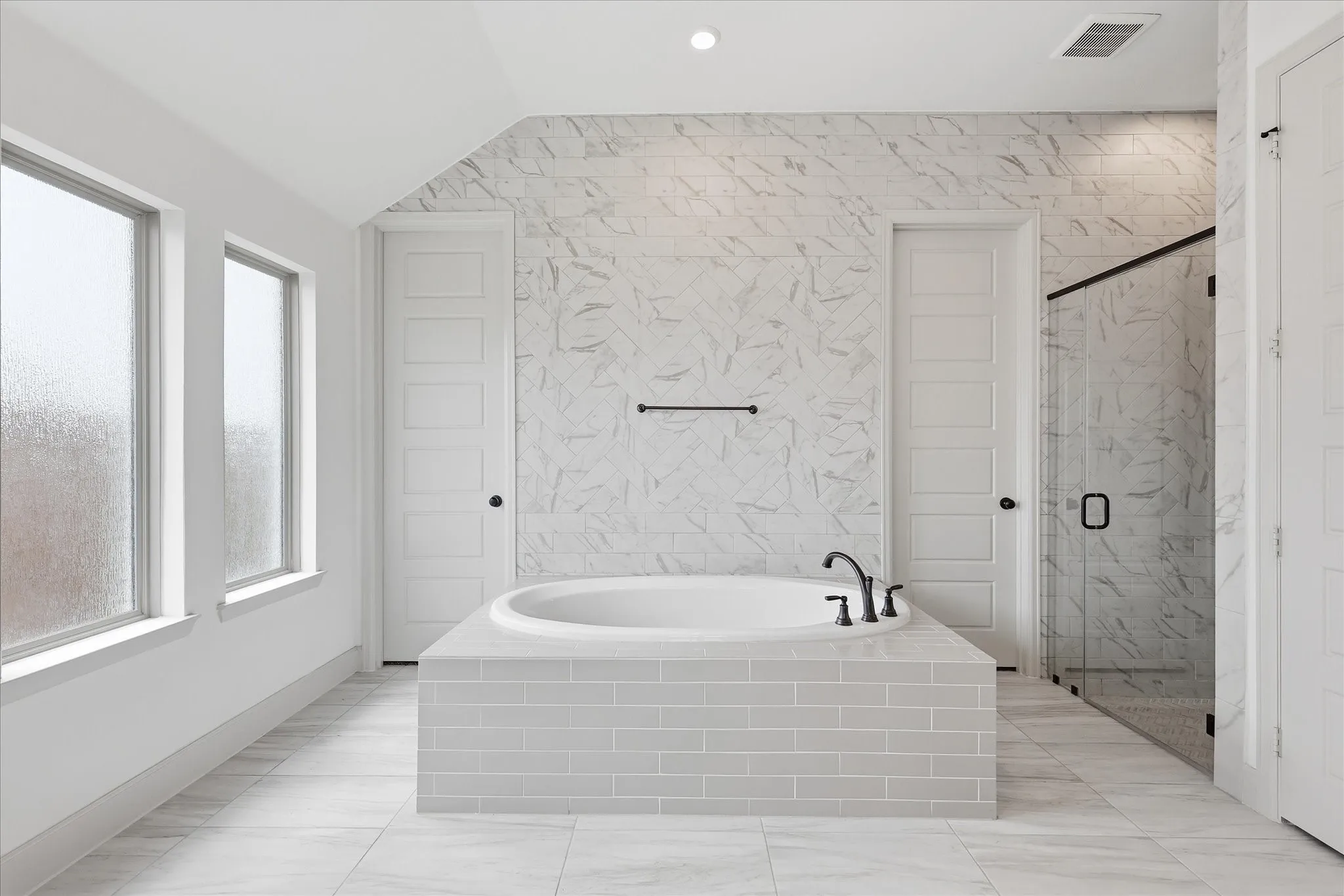 Built-in soaking tub with matte black fixtures, surrounded by subway tile and a marble-look tiled accent wall