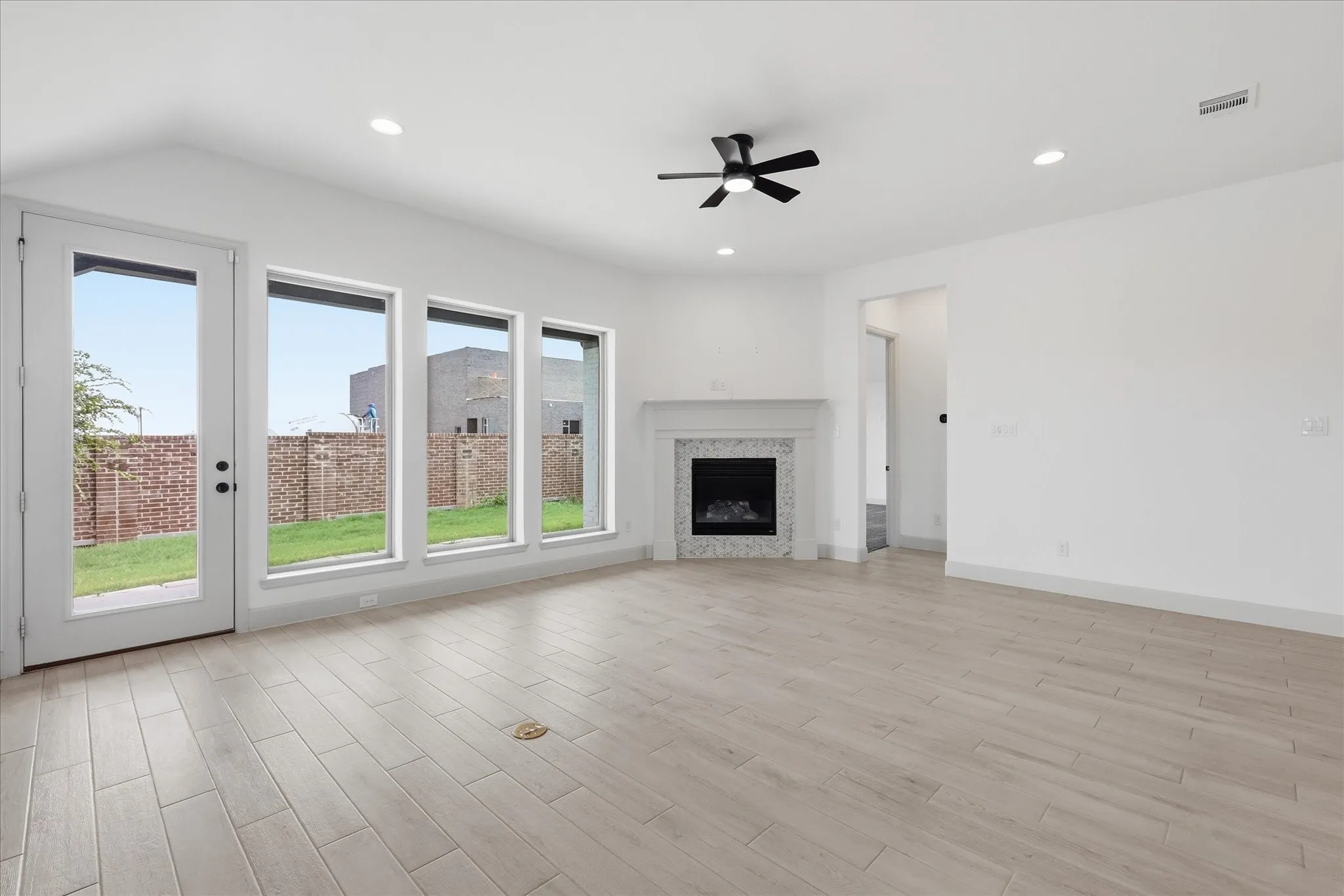 Spacious living area featuring light wood-finish flooring, a contemporary fireplace with a decorative mantel, and recessed lighting