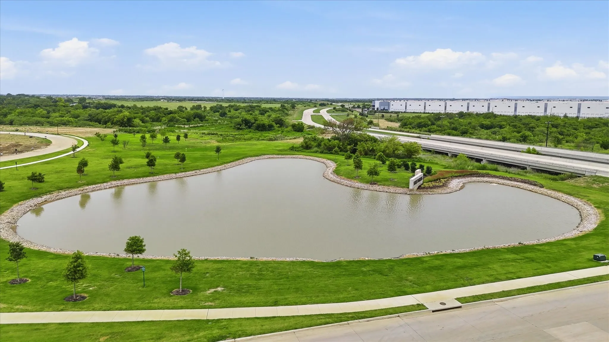 Pond feature with surrounding green space, paved pathways, and mature landscaping