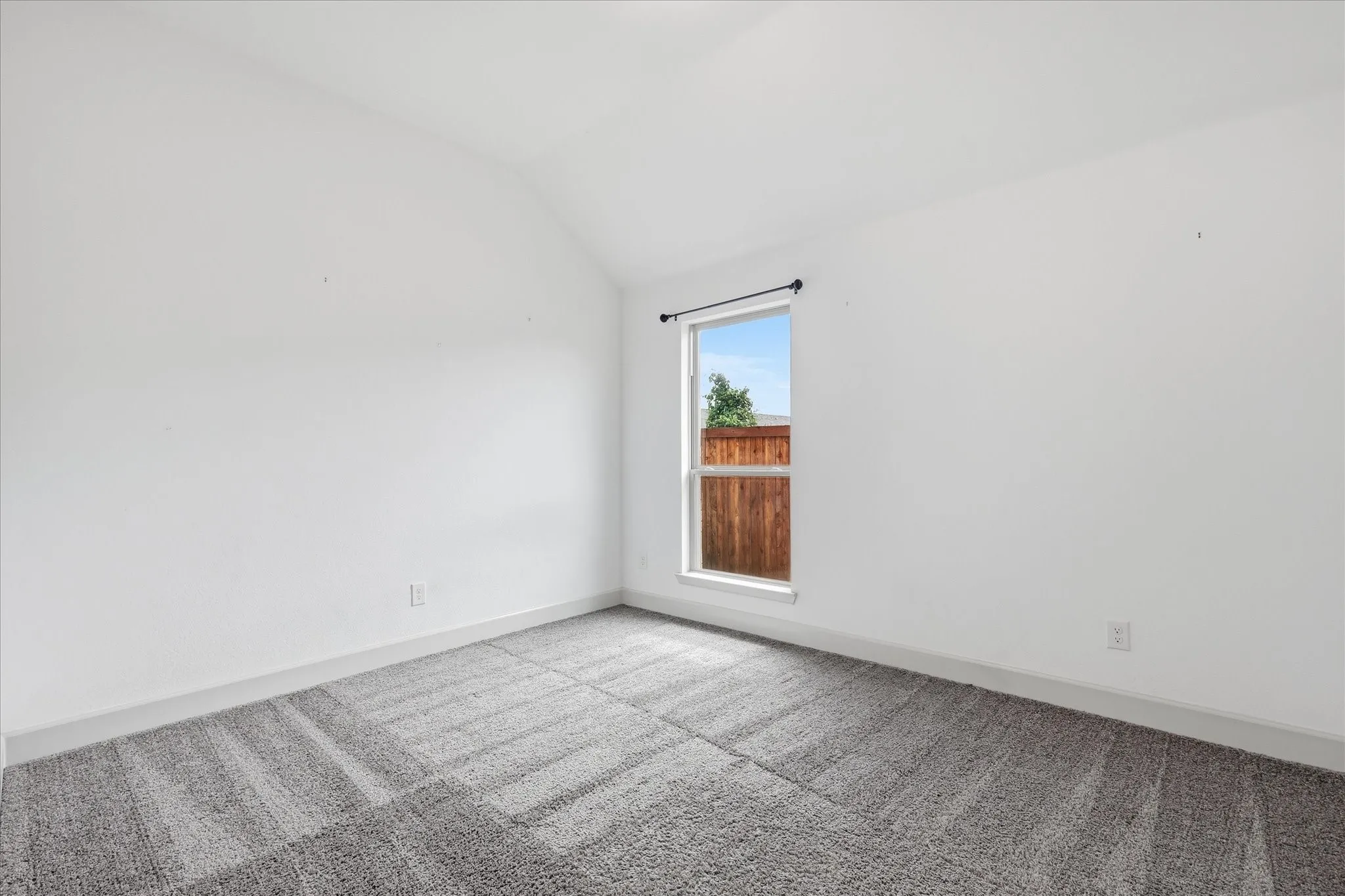 Bright interior space featuring a window with natural light, textured carpeting, white walls, and a neutral baseboard trim