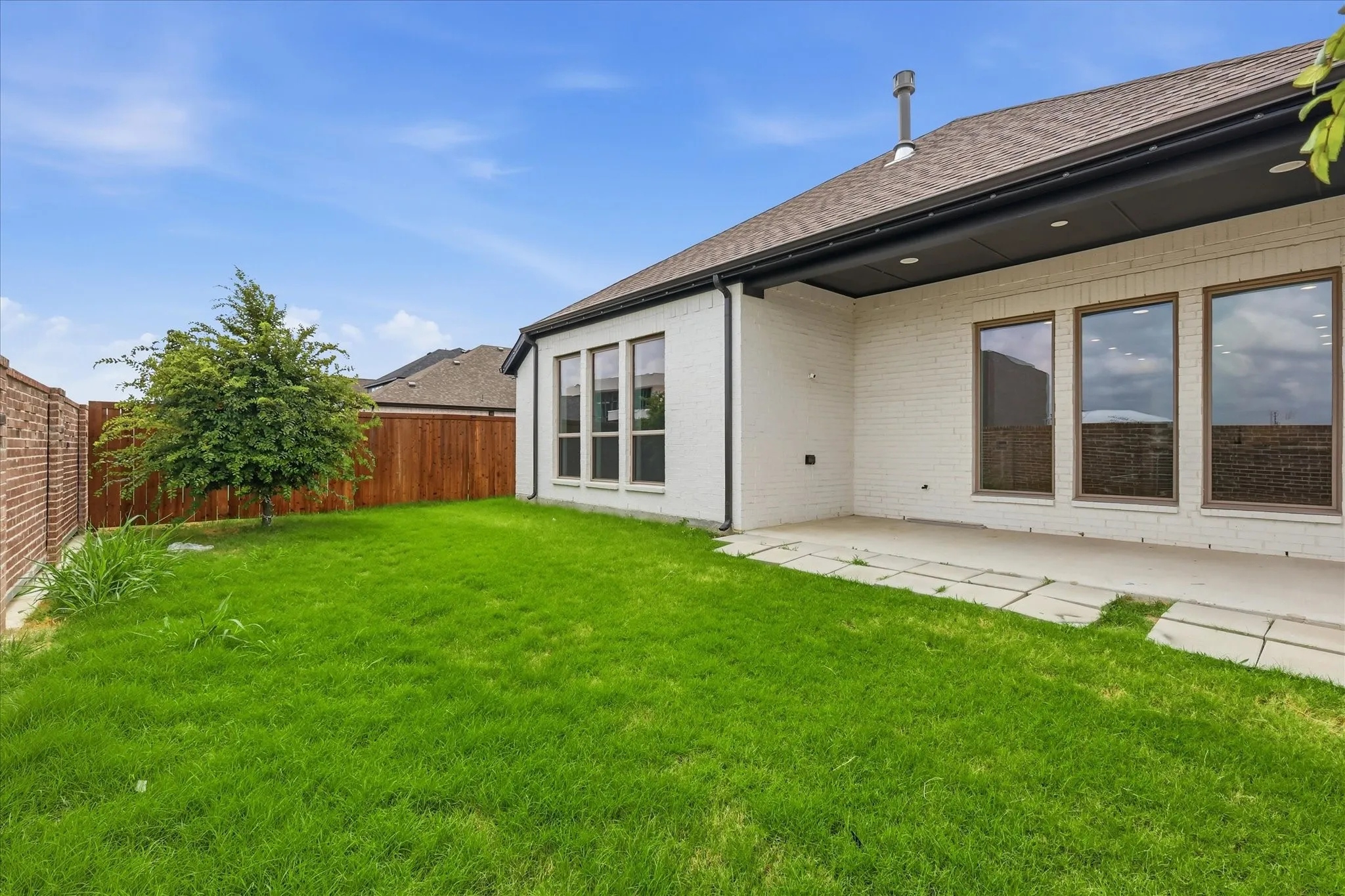 Expansive backyard featuring a lush green lawn, a mature tree, and a concrete patio