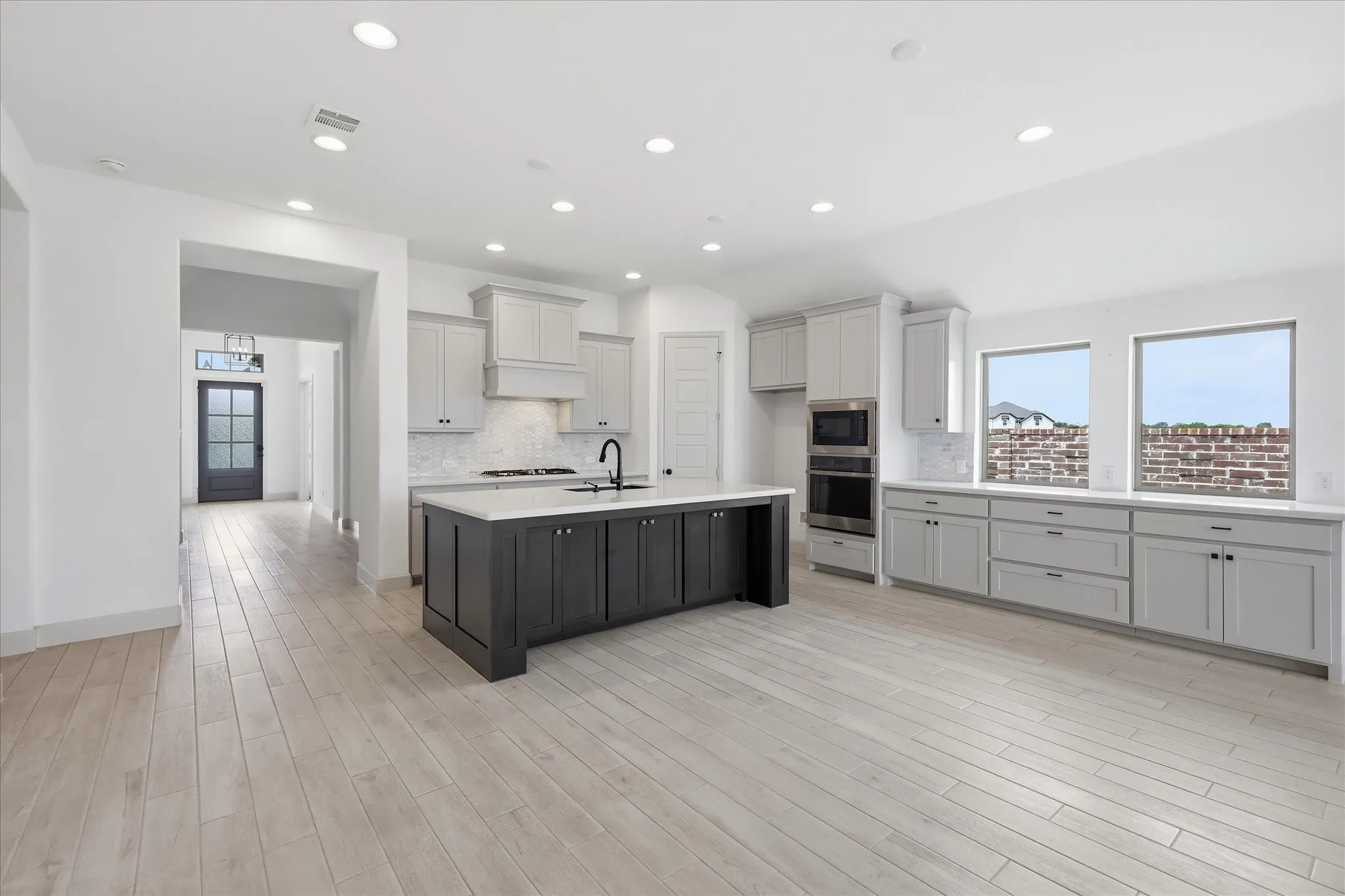 Open-concept kitchen featuring wood-finish flooring, a central island with dark cabinetry, light-toned perimeter cabinetry, integrated stainless steel appliances, and multiple windows