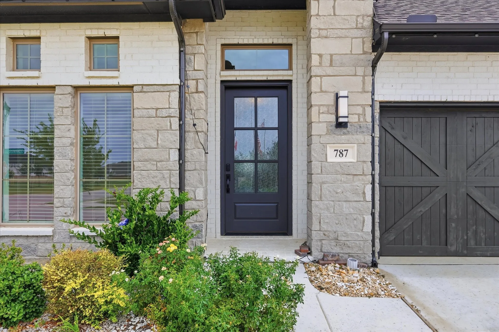 Modern exterior featuring a dark paneled entry door with glass inserts, light-toned stone and brick facade, a contemporary outdoor light fixture, and a dark wood-finish garage door