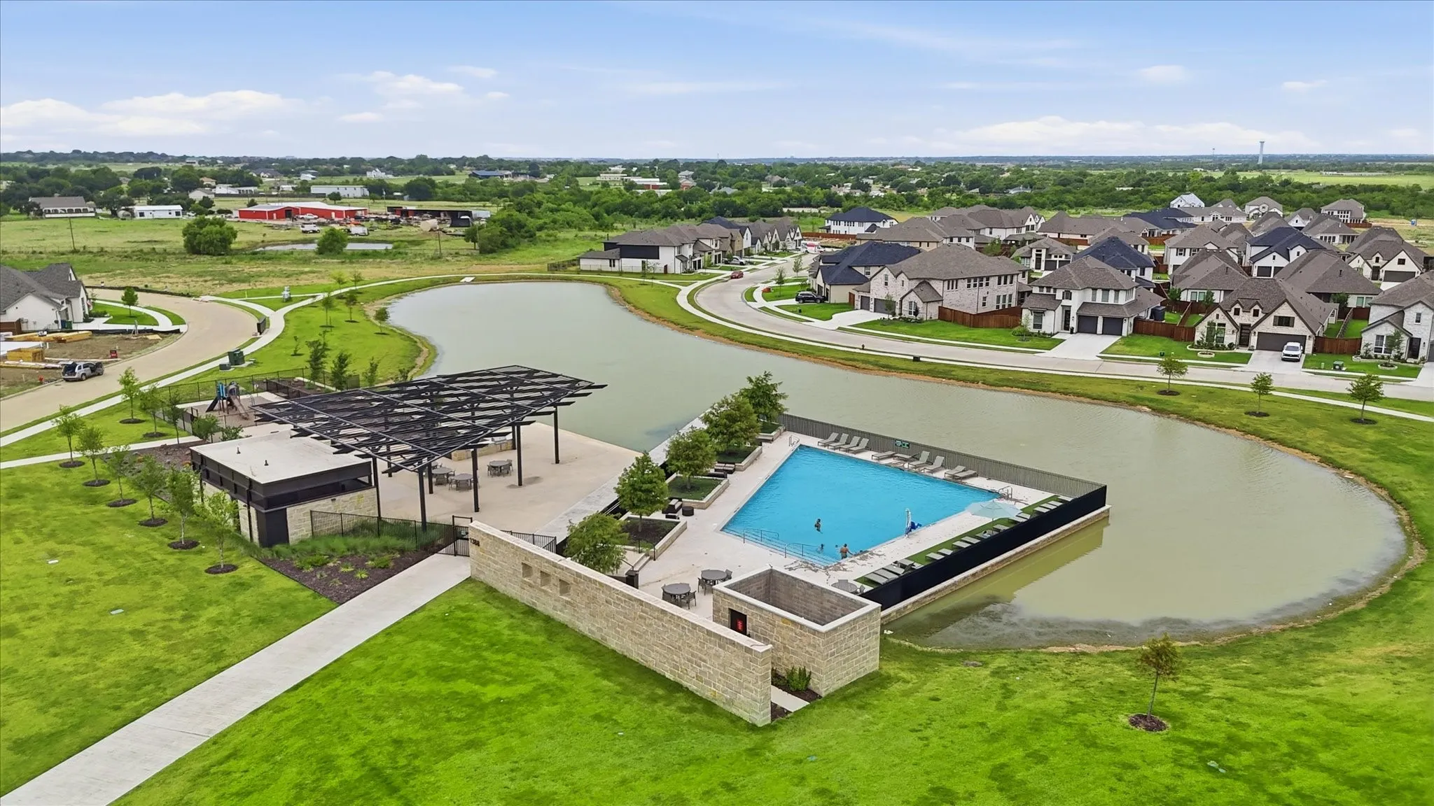 Resort-style community pool with surrounding lounge chairs, an adjacent covered patio area, and a stone-clad building