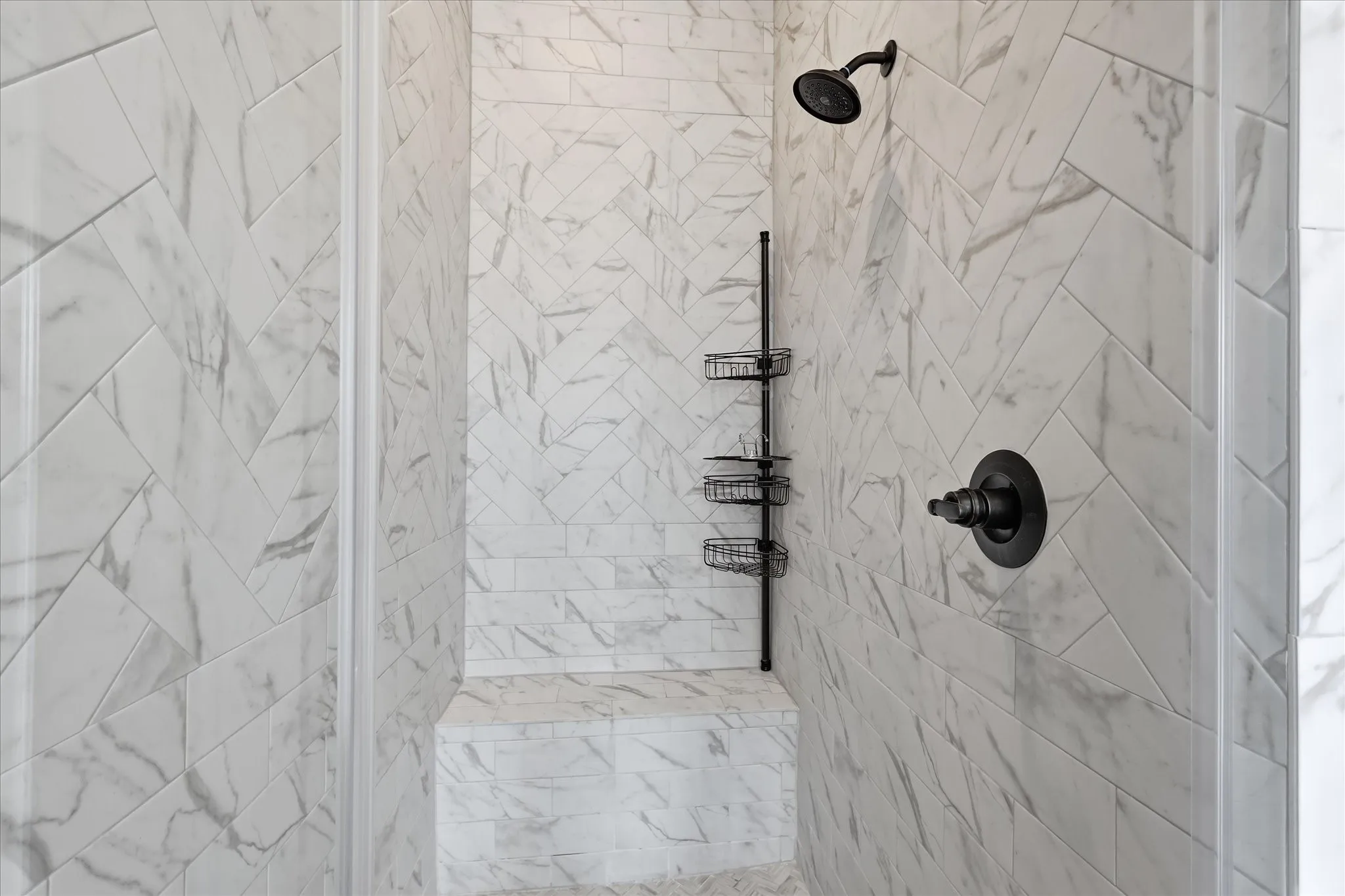 Shower stall featuring herringbone-patterned tile, integrated bench seating, and matte black fixtures