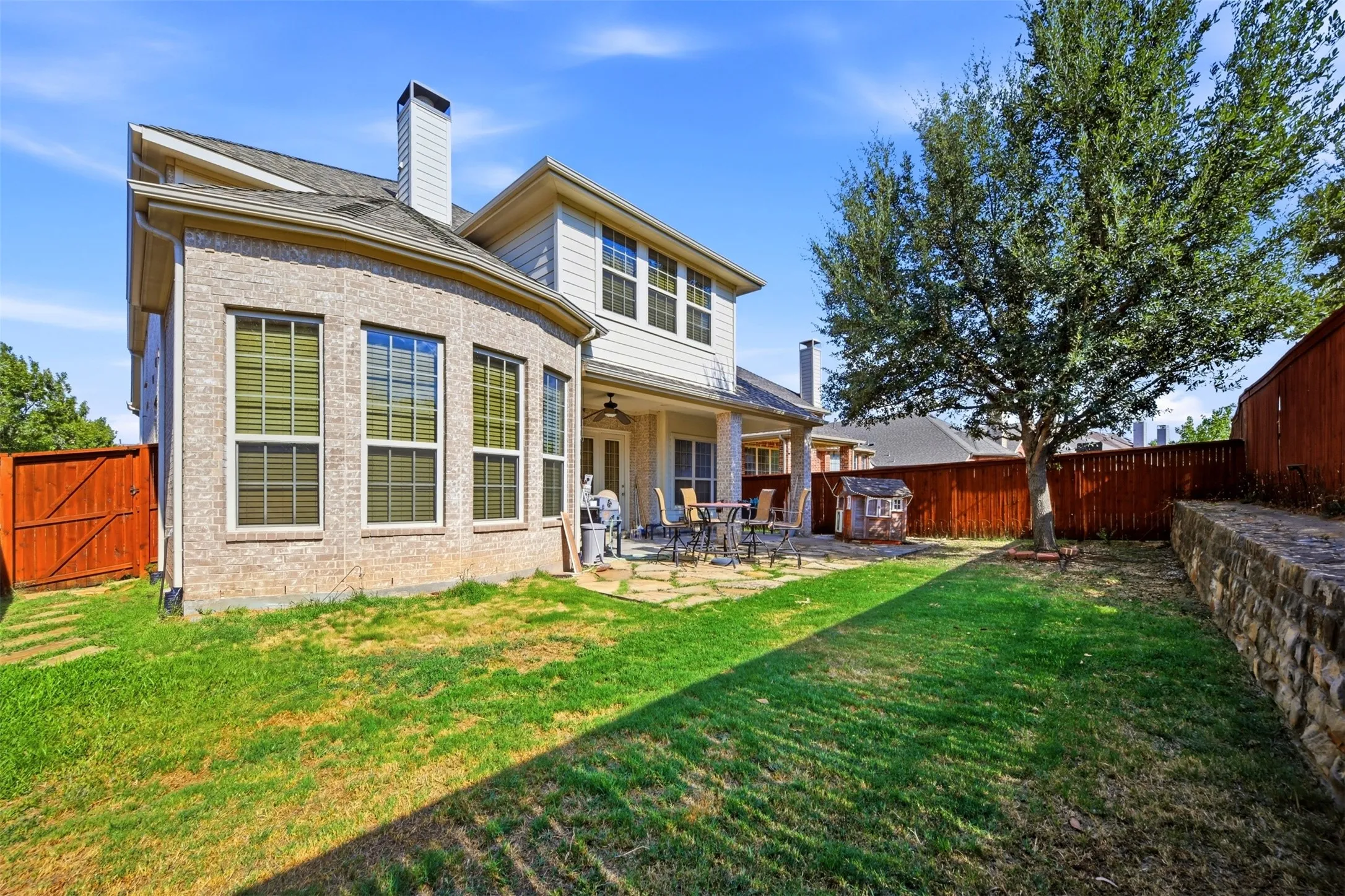 Exterior featuring a brick and siding facade, covered patio with recessed lighting, stone retaining wall, and a wood privacy fence