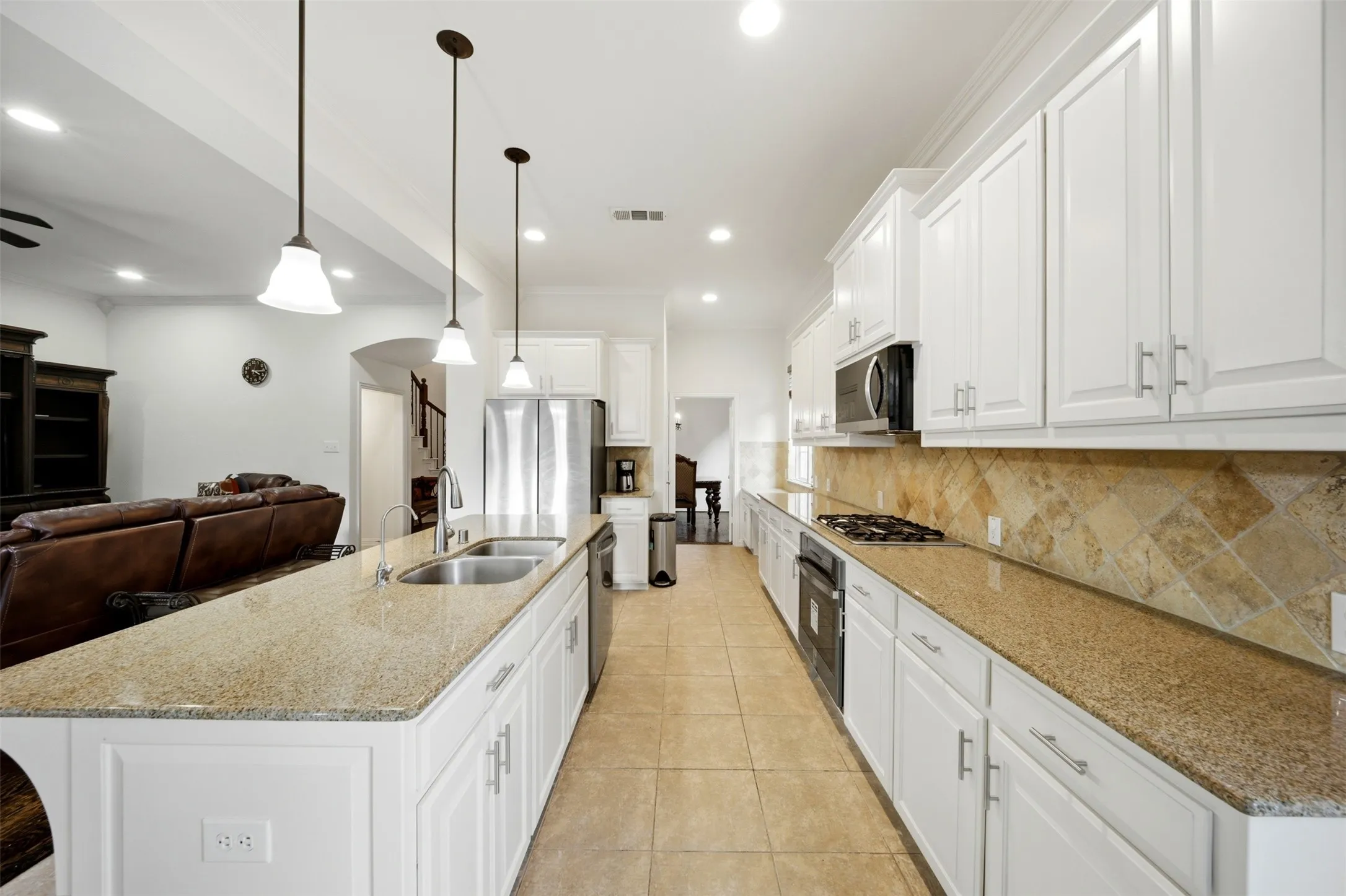 Kitchen featuring an expansive island with a double basin sink, white cabinetry with silver-tone hardware, a gas cooktop, built-in oven, and tile flooring