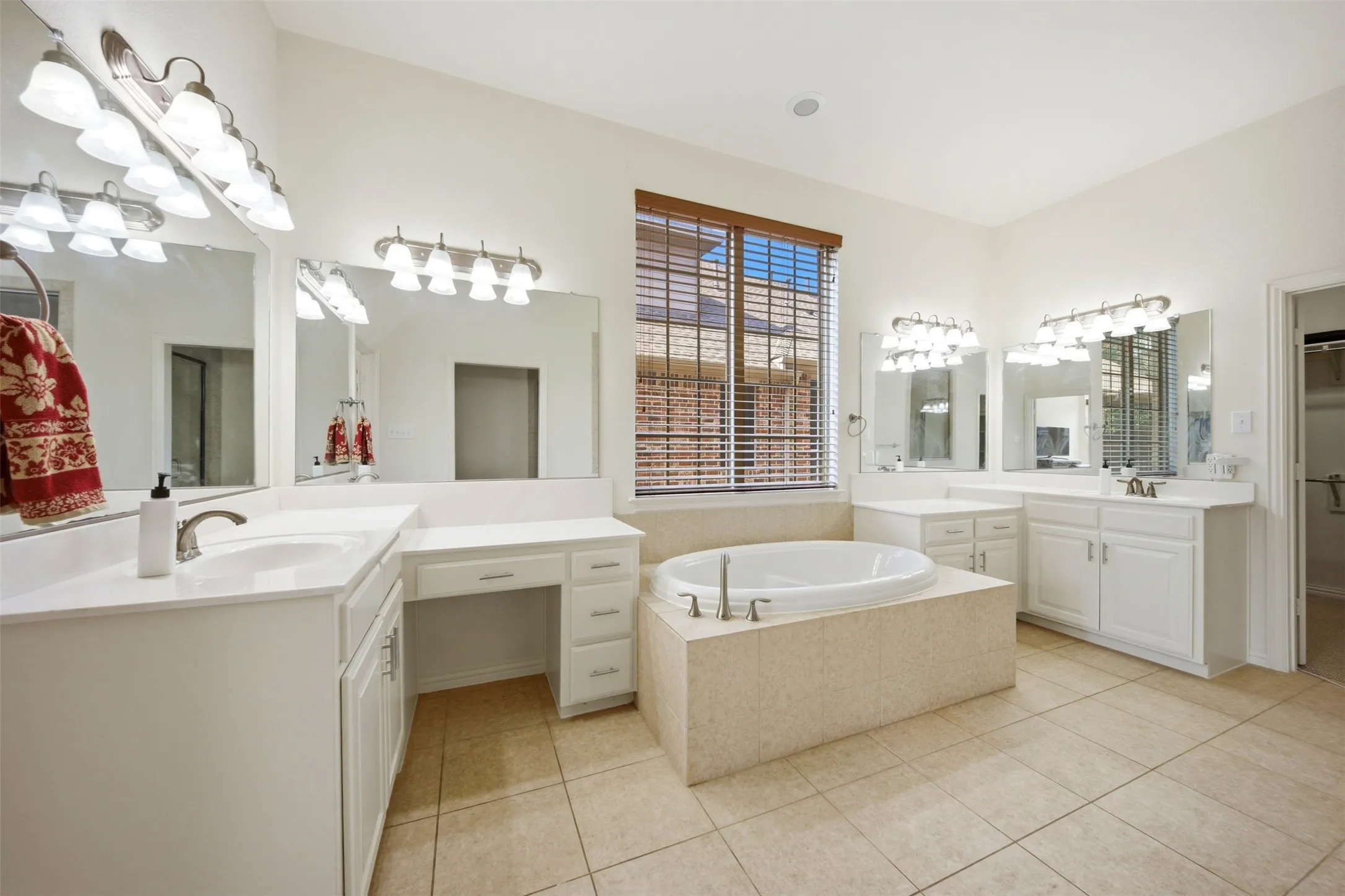 Dual vanities with white cabinetry, a built-in makeup desk, an oval soaking tub, and tile flooring