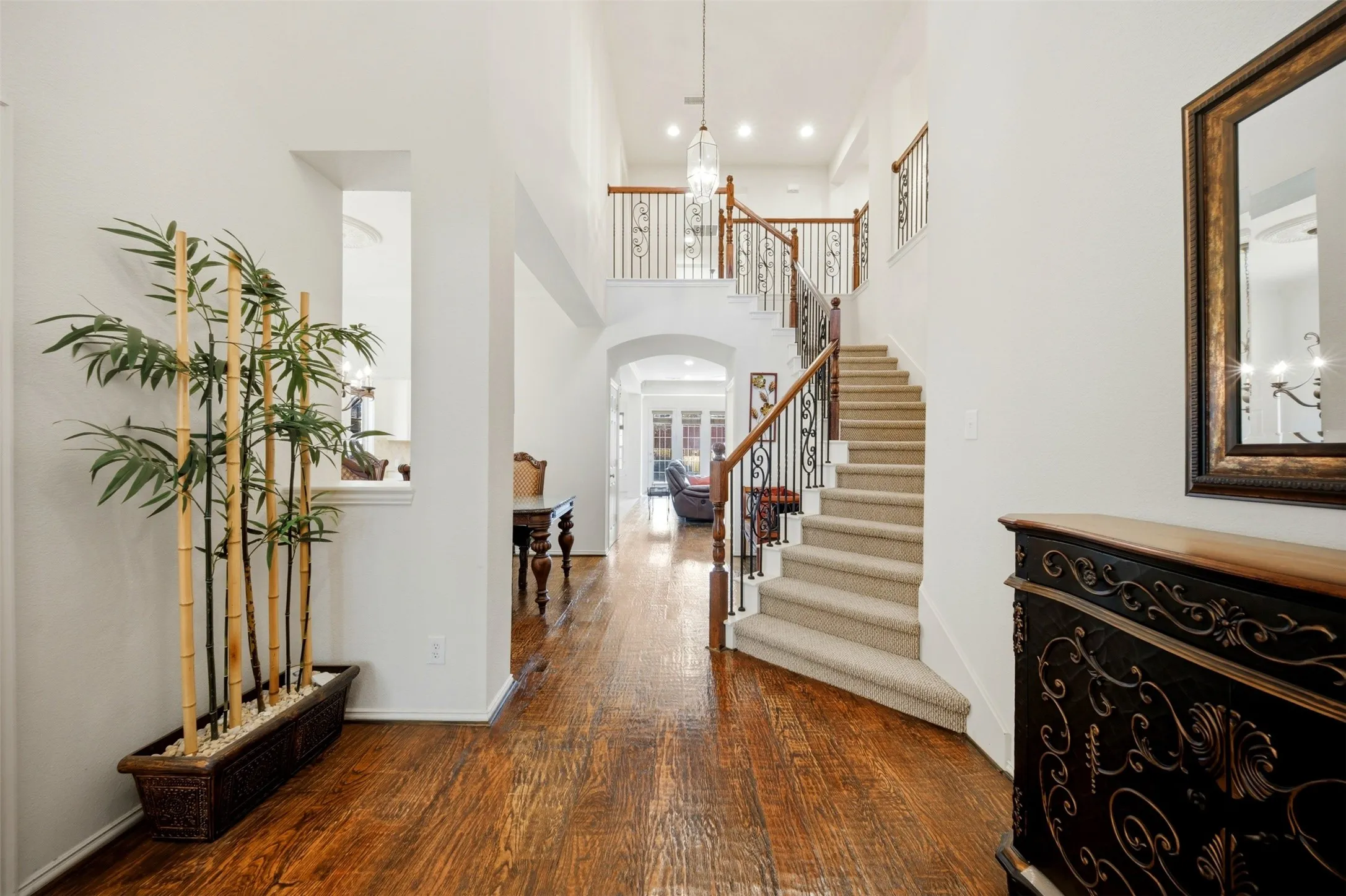 Two-story entryway with wood-finish flooring, a carpeted staircase with wrought iron and wood railings, and a hanging chandelier