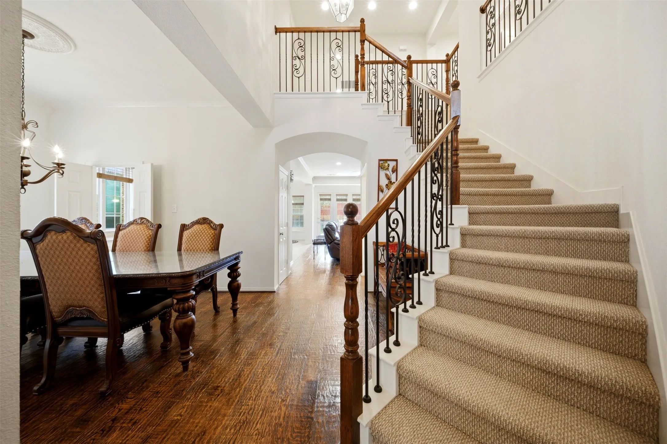 Hardwood flooring, grand staircase with decorative wrought iron spindles, high ceilings, arched doorways, and a formal dining area