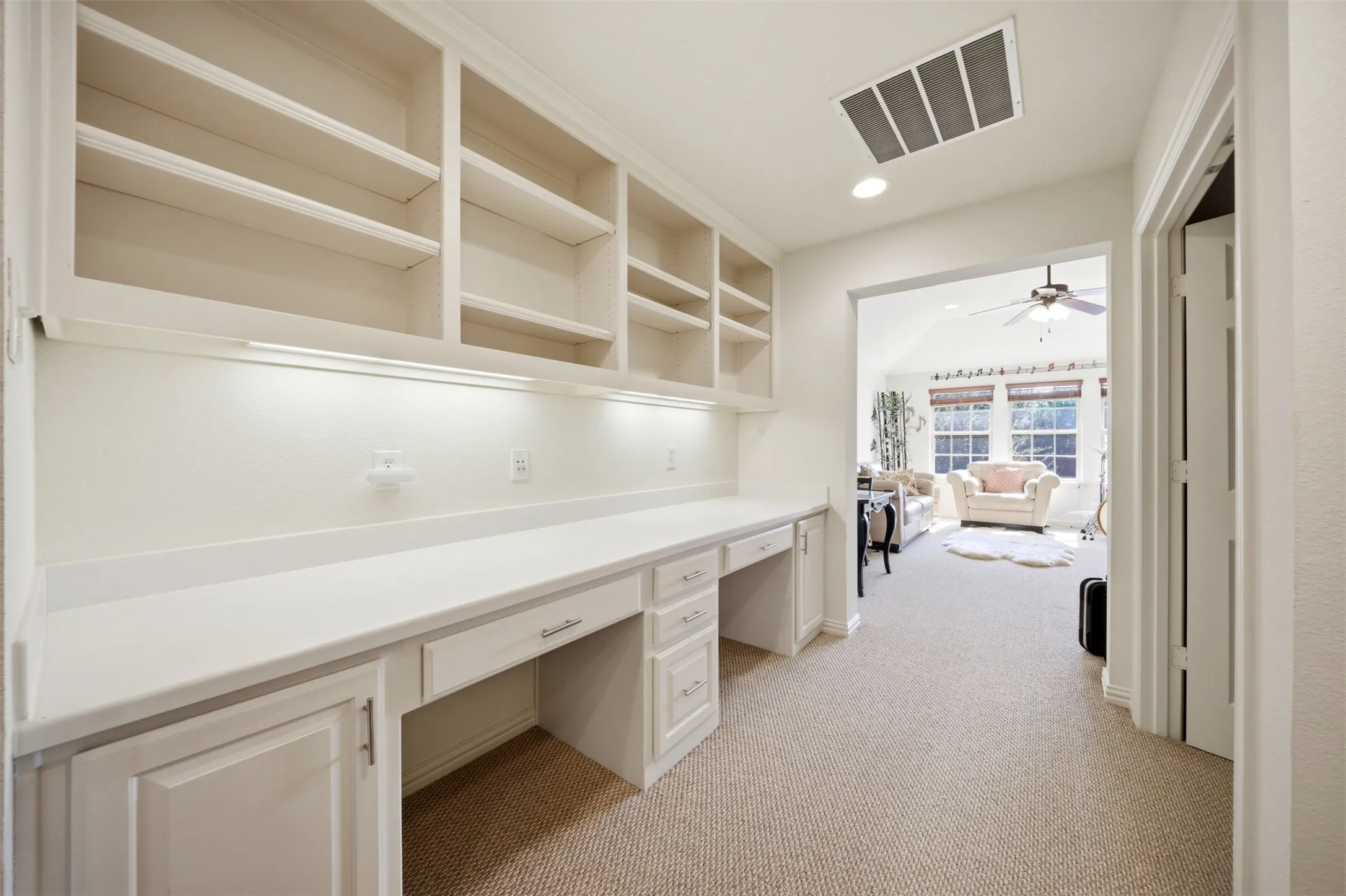 Built-in desk area featuring integrated shelving, under-cabinet lighting, multiple workstations, and carpet flooring