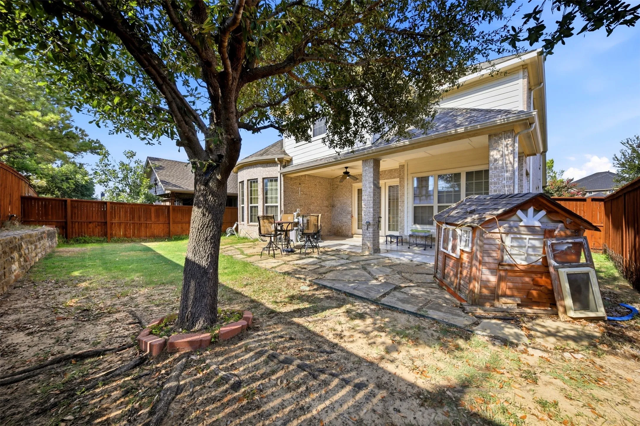 Expansive backyard featuring a stone patio, covered porch with ceiling fan, and a wood privacy fence
