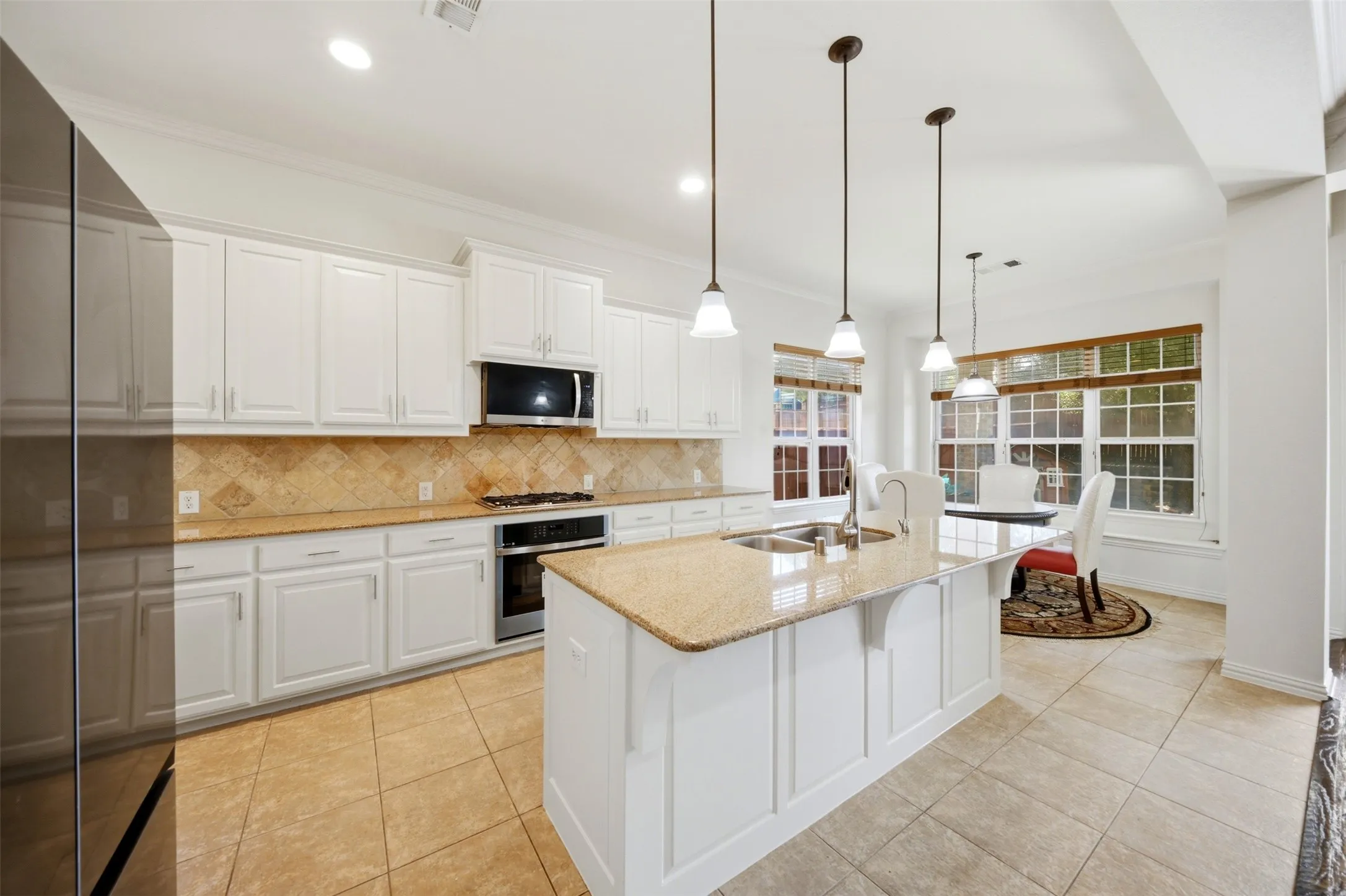 White cabinetry, stainless steel appliances, granite countertops, tile flooring, and multiple windows