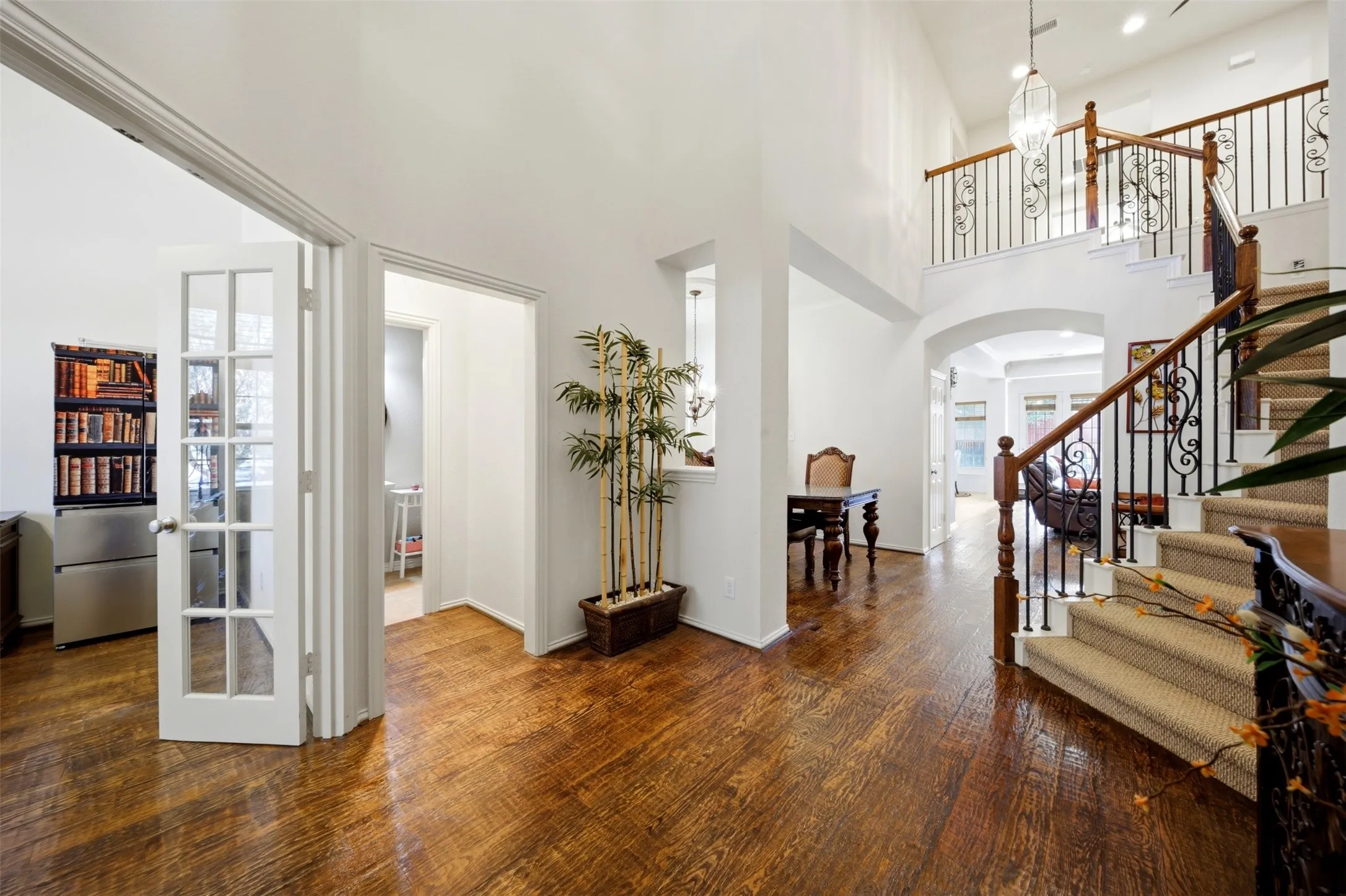 Wood-finish flooring throughout, featuring a grand staircase with wrought iron balusters and wood handrails, a two-story entry, an arched doorway, and French doors