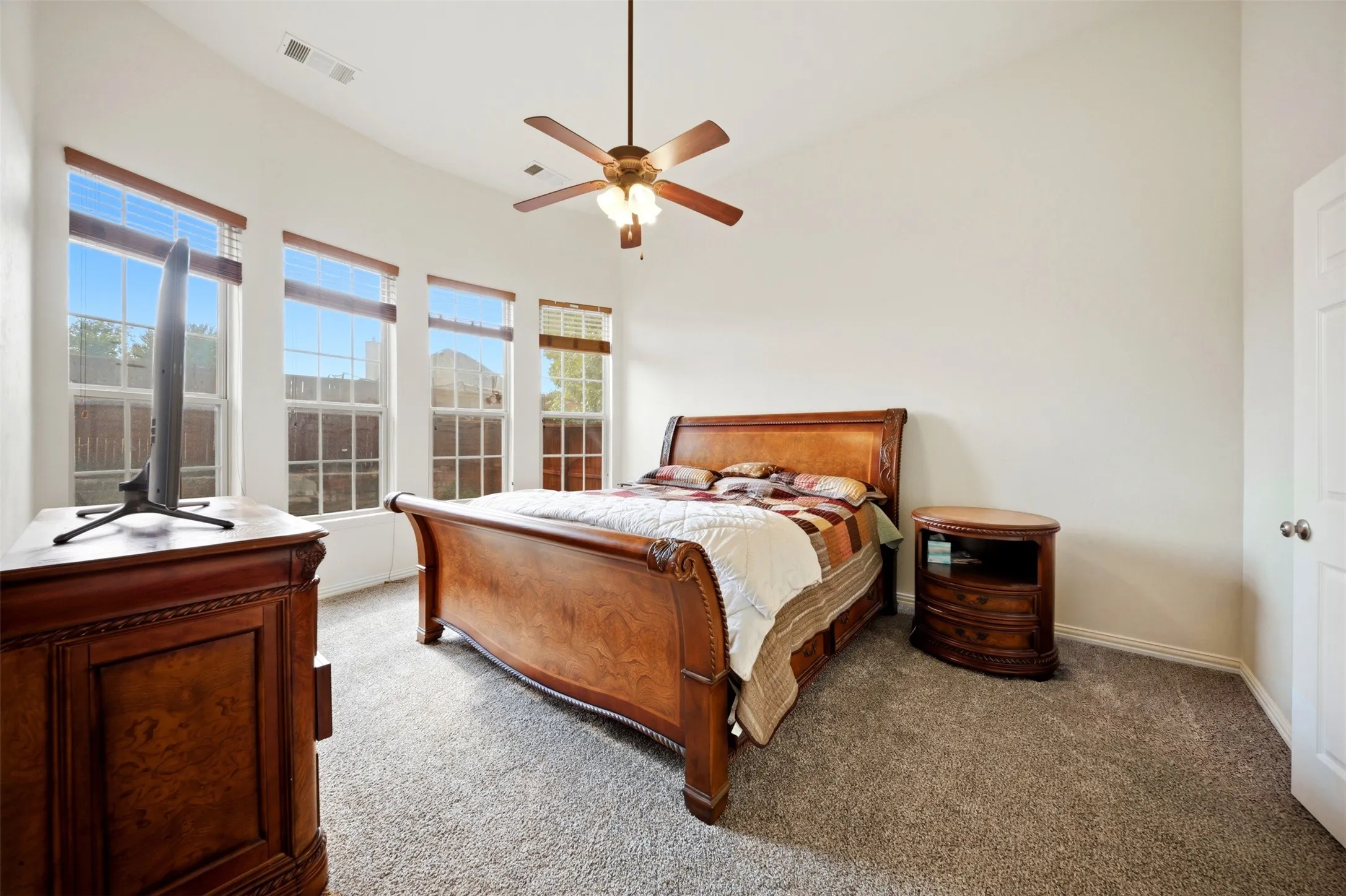 Vaulted ceiling, multiple windows with window treatments, ceiling fan, neutral wall paint, and gray carpet flooring