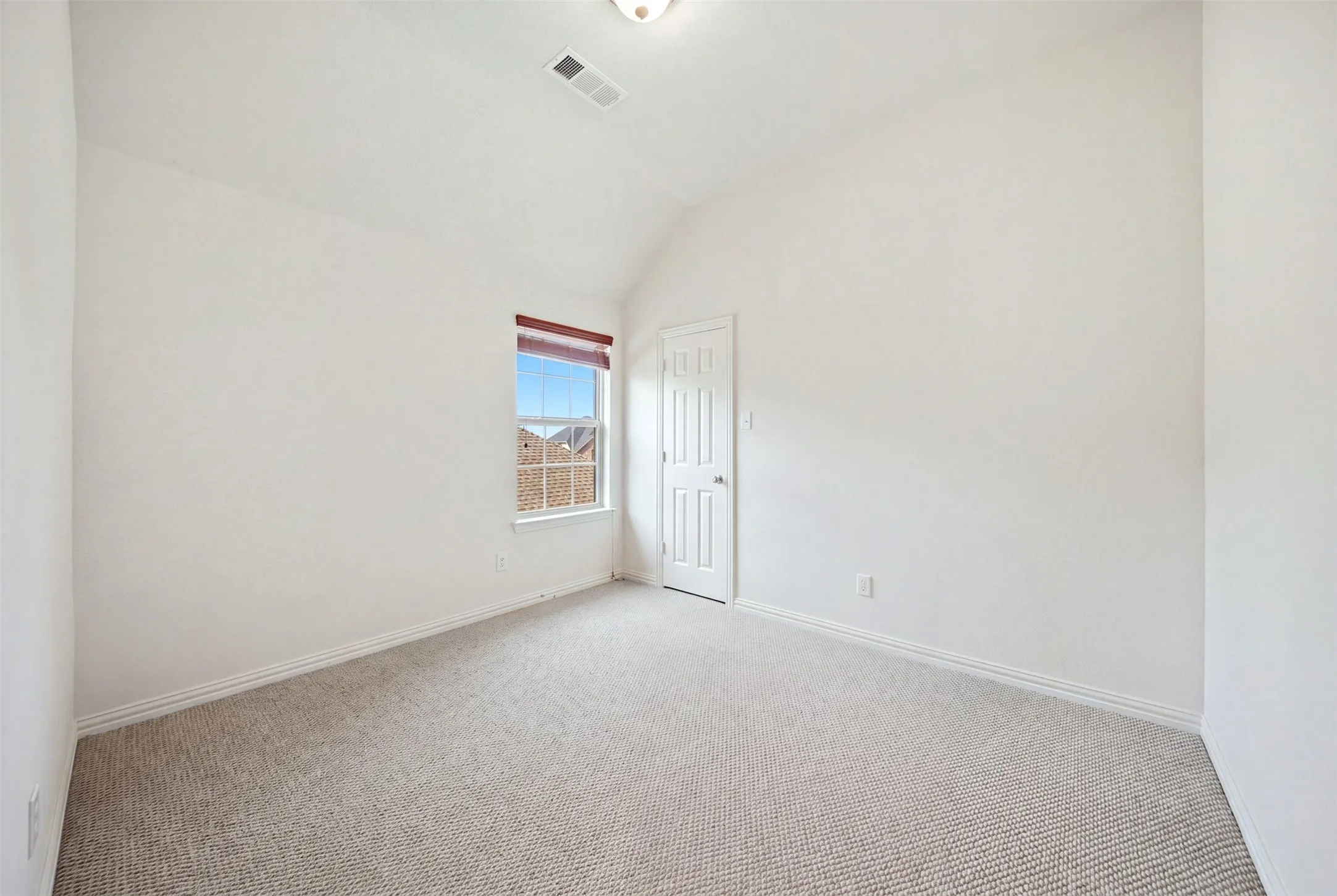 Neutral carpeting, white painted walls, vaulted ceiling, and a single window with a blind