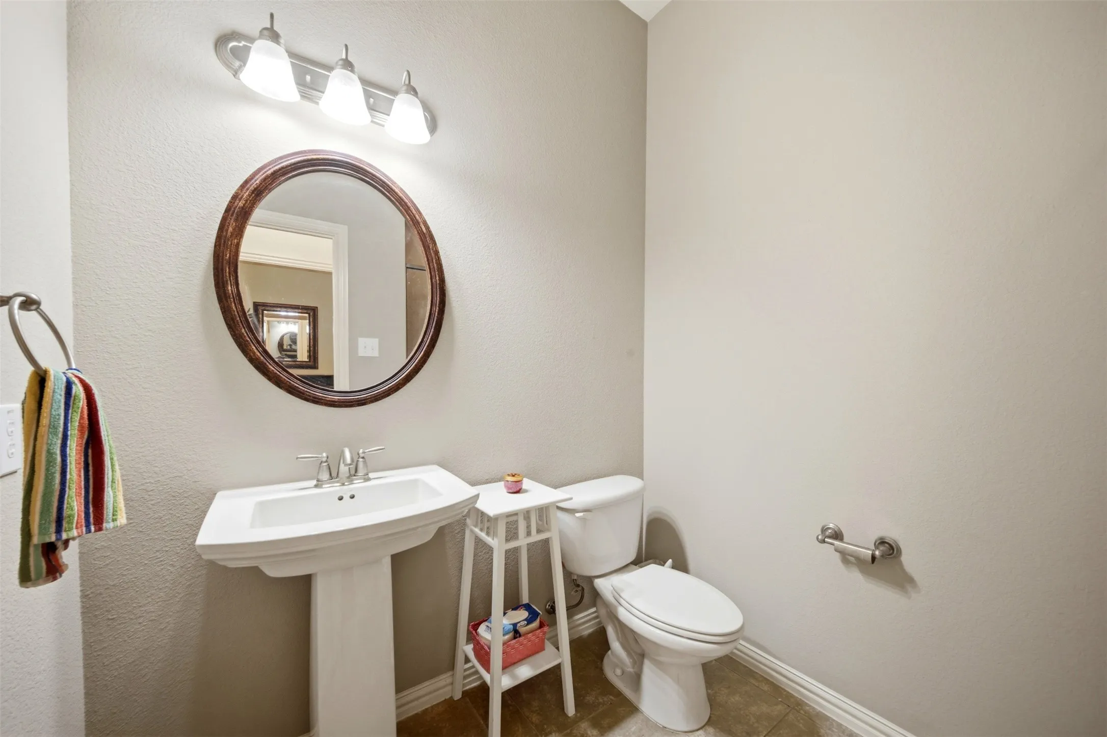 Pedestal sink with chrome faucet, oval wood-framed mirror, and a three-light vanity fixture