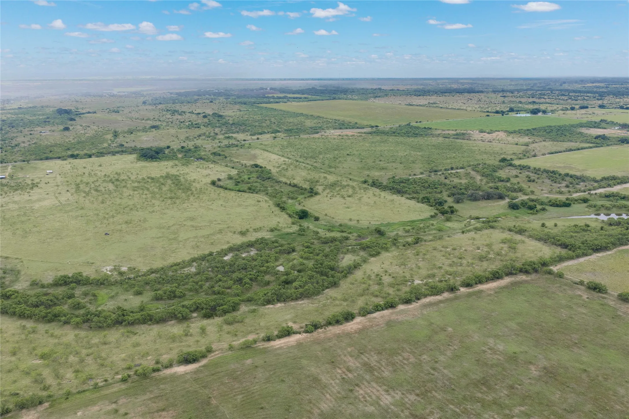 Expansive rural landscape featuring a mix of green pastures and dense brushland