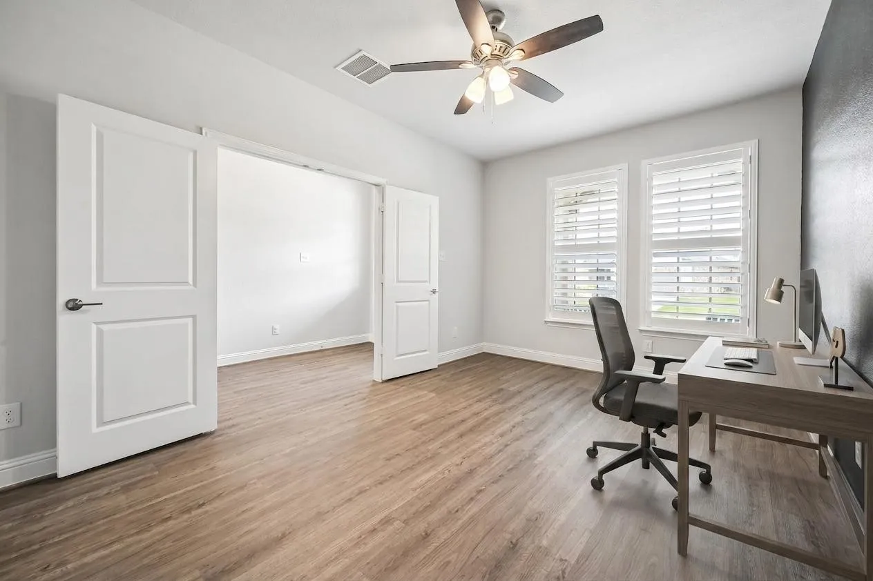 Versatile room featuring wood-finish flooring, a ceiling fan, and two windows with plantation shutters