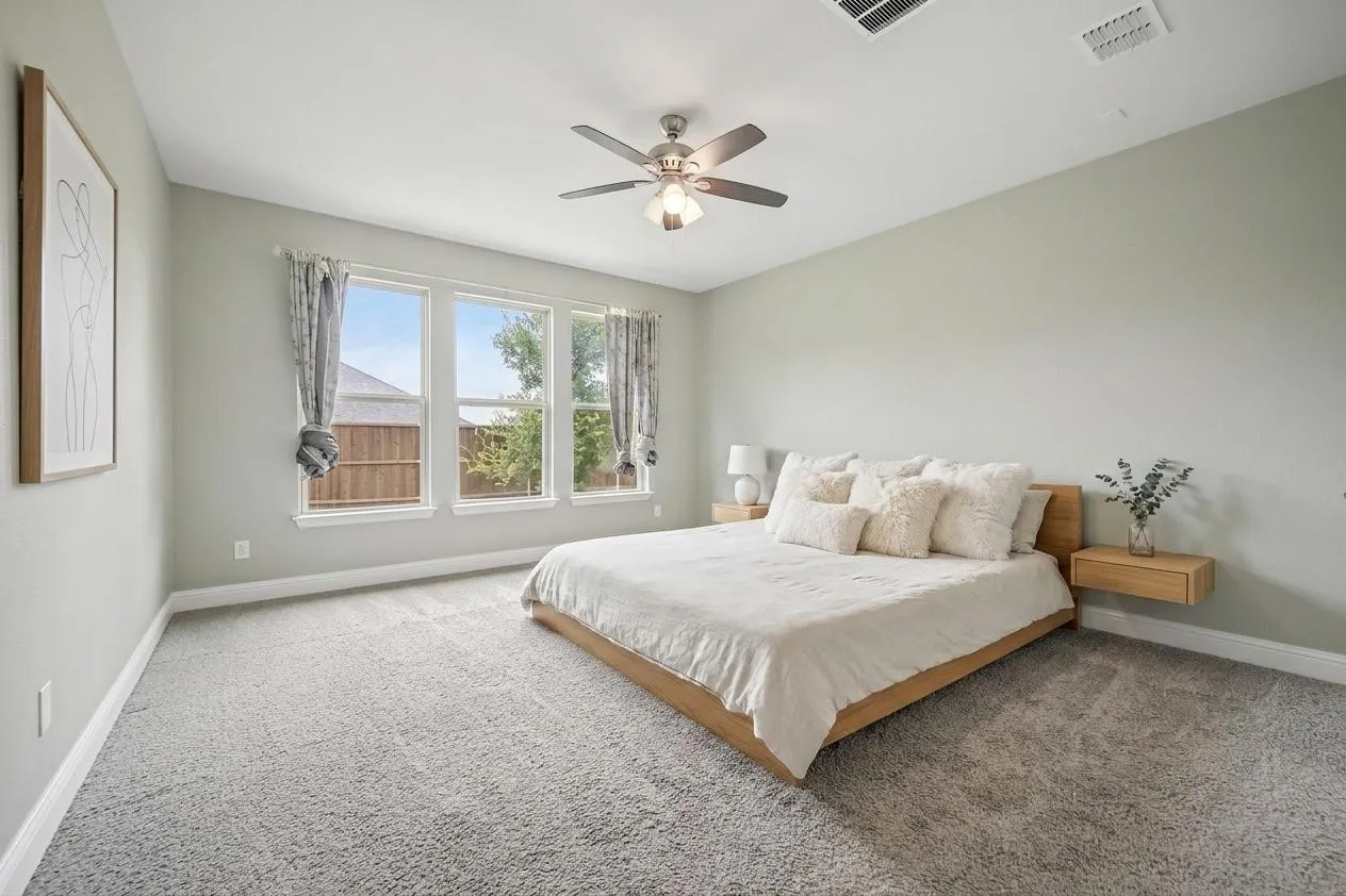 Spacious room featuring light gray carpet flooring, three large windows with white trim, a ceiling fan with integrated lighting, and neutral wall paint