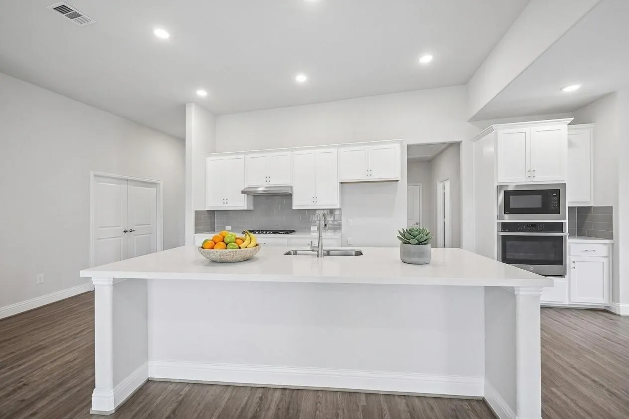 Modern kitchen featuring a white island with sink, stainless steel appliances, white cabinetry, and wood-finish flooring