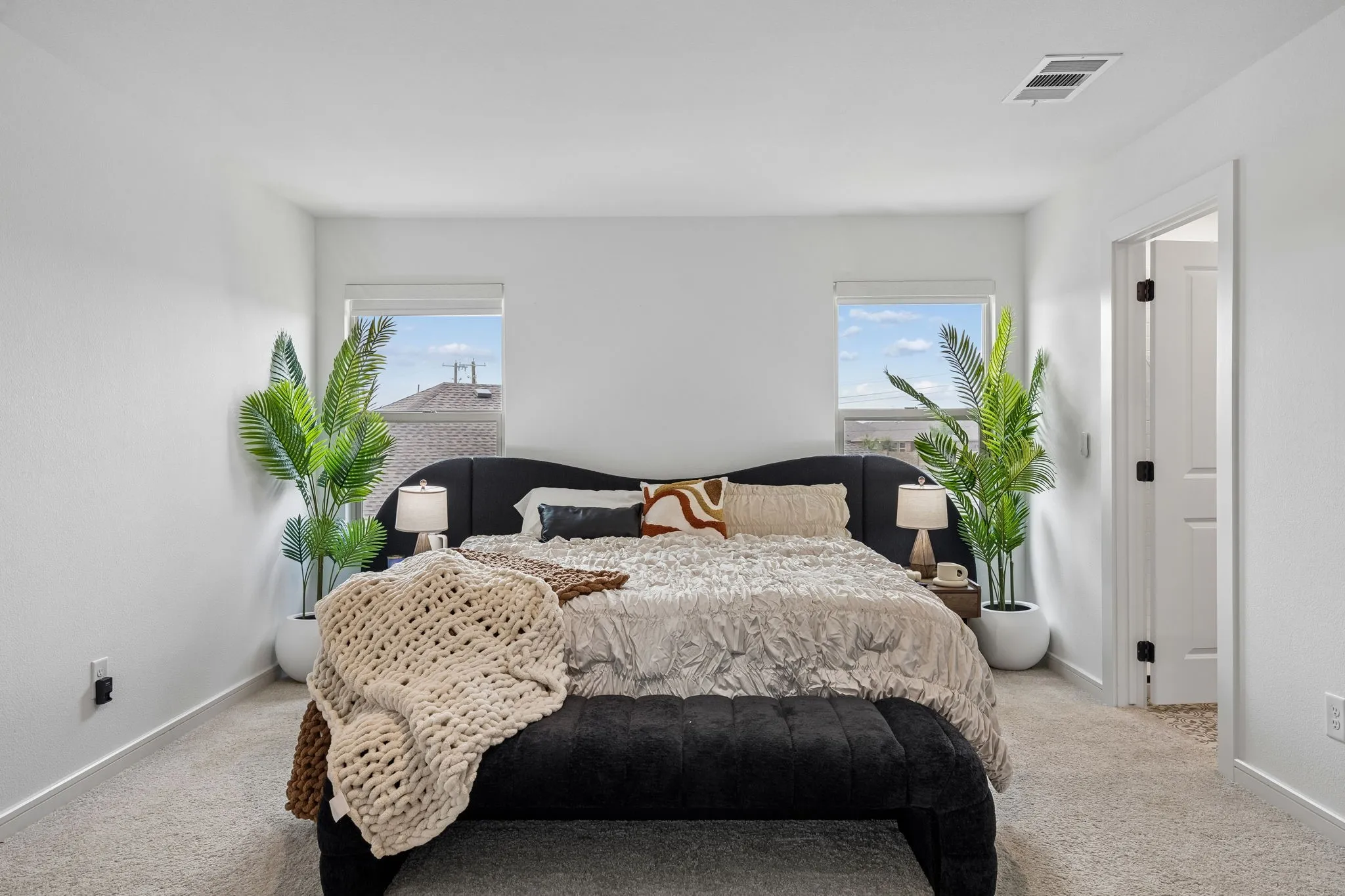 Bright interior space featuring a recessed ceiling vent, light-toned carpeting, and a white paneled door with dark hardware