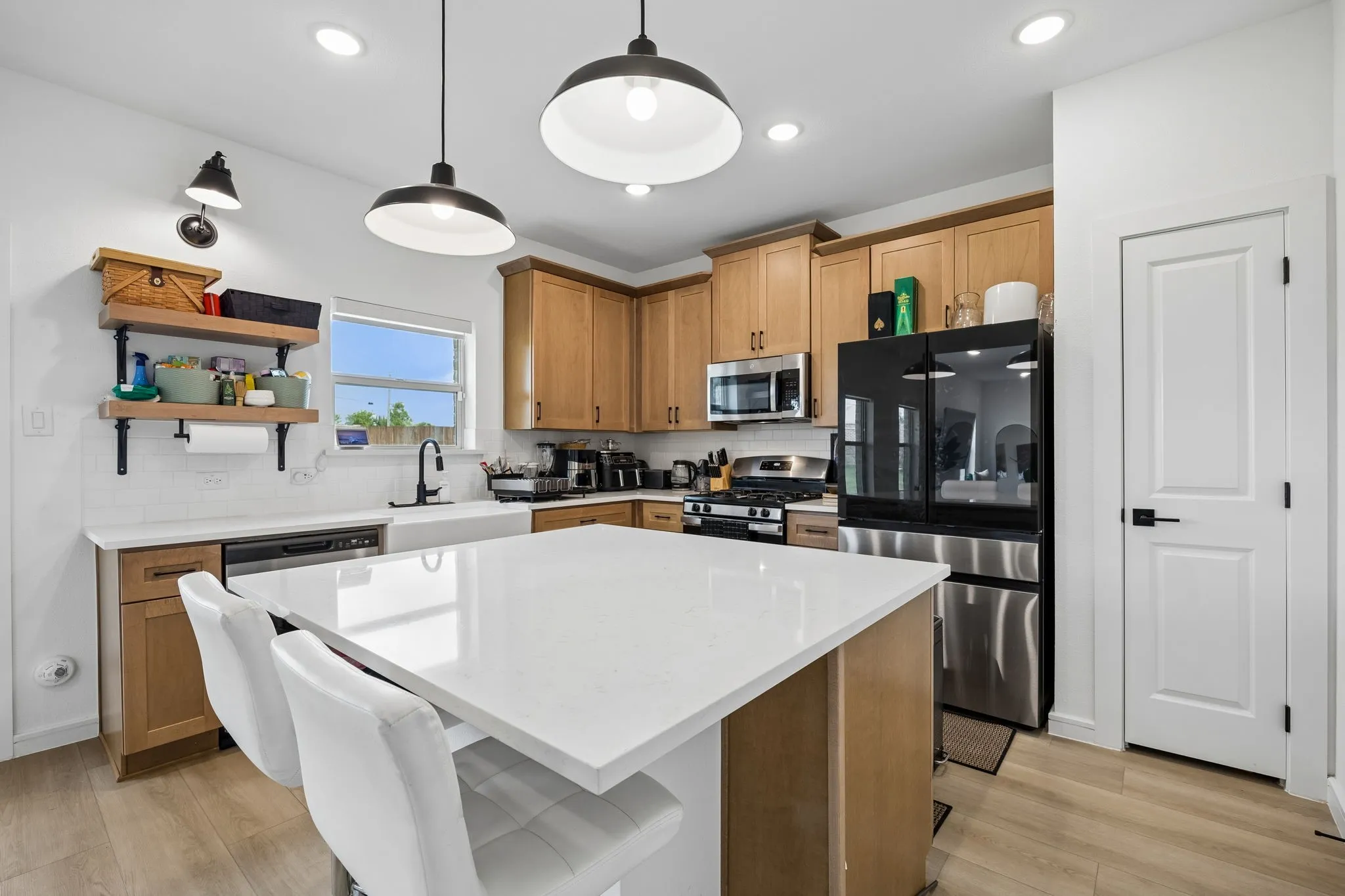 Kitchen featuring a large central island with white countertop, recessed lighting, wood-finish flooring, light wood cabinetry, and stainless steel appliances
