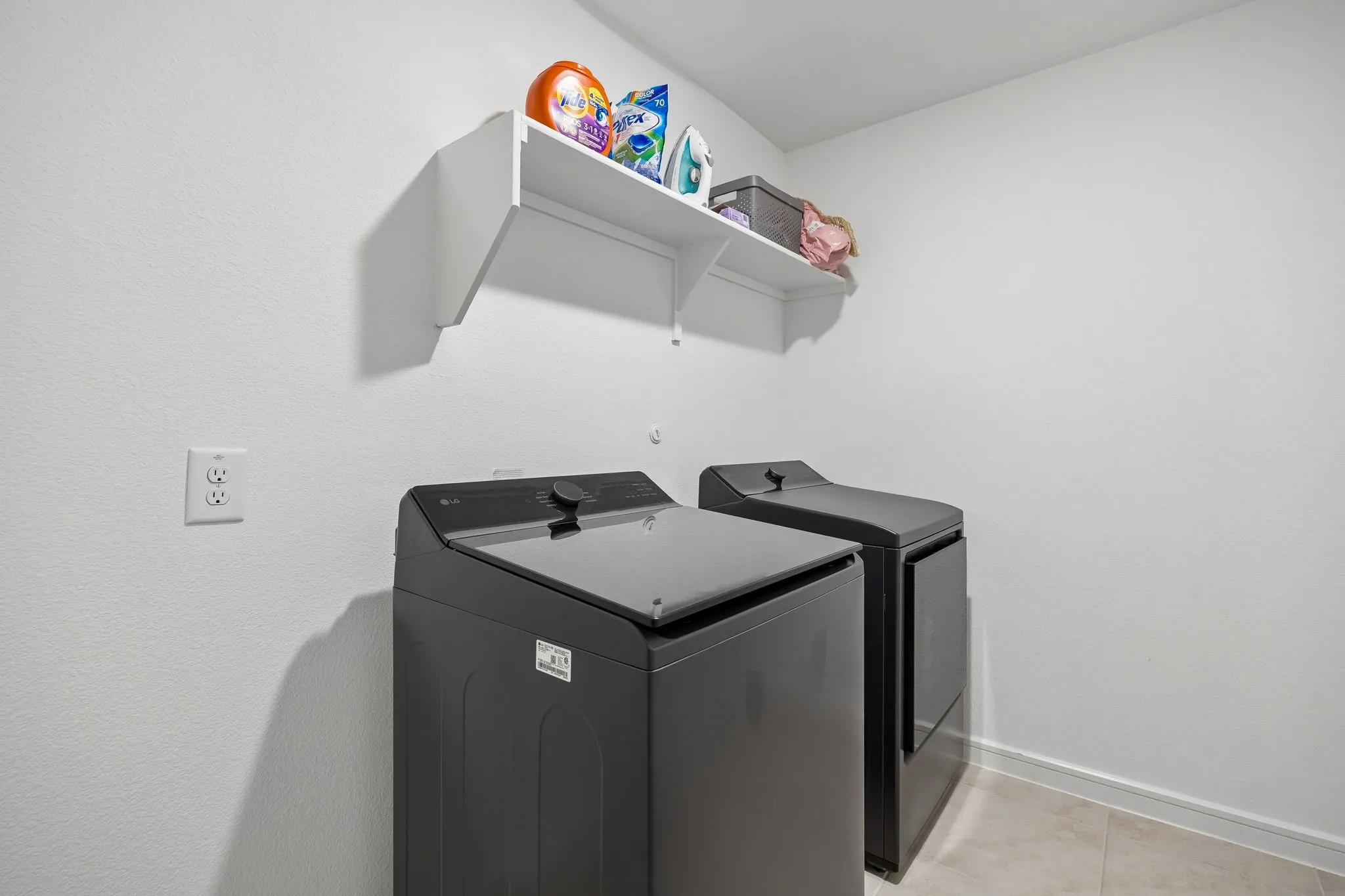 Dedicated laundry area featuring a wall-mounted shelf, light-colored walls, and tile flooring