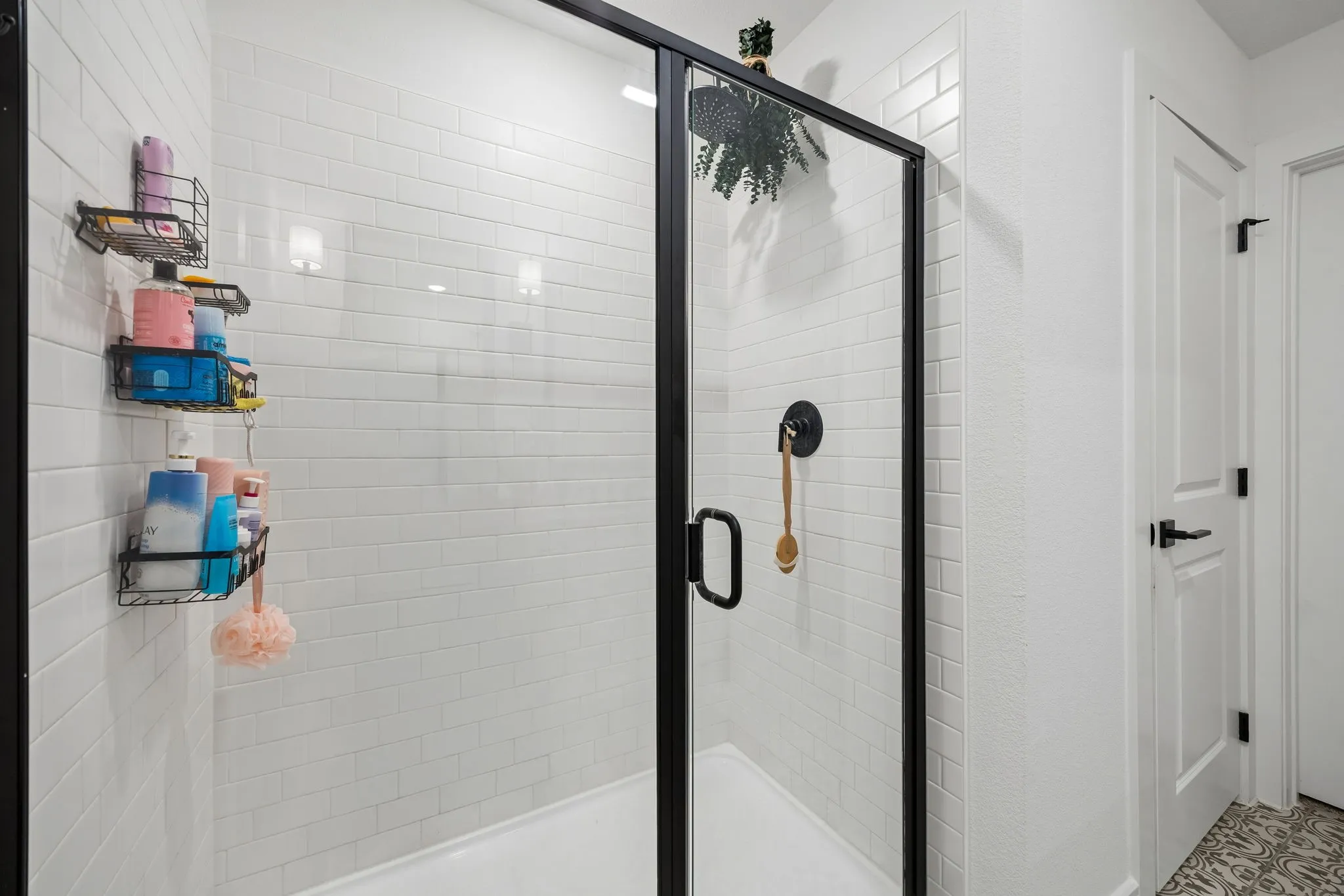 Walk-in shower featuring a frameless glass enclosure with black trim, white subway tile surround, and a matte black shower fixture
