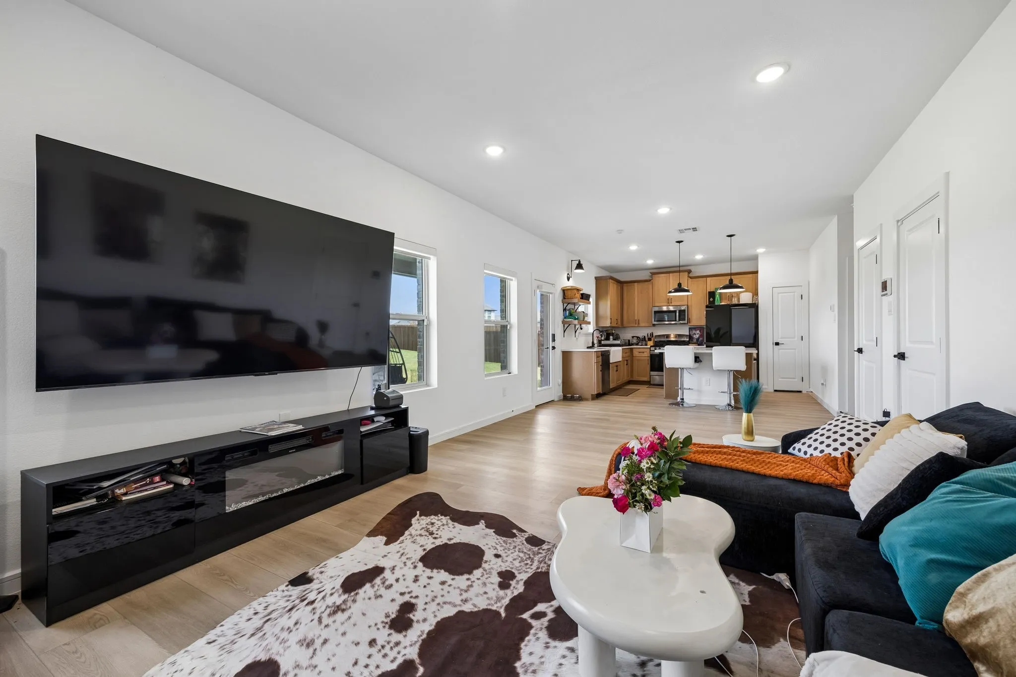 Open-concept living space featuring light wood-finish flooring, recessed lighting, and a kitchen with wood cabinetry, black appliances, and pendant lighting