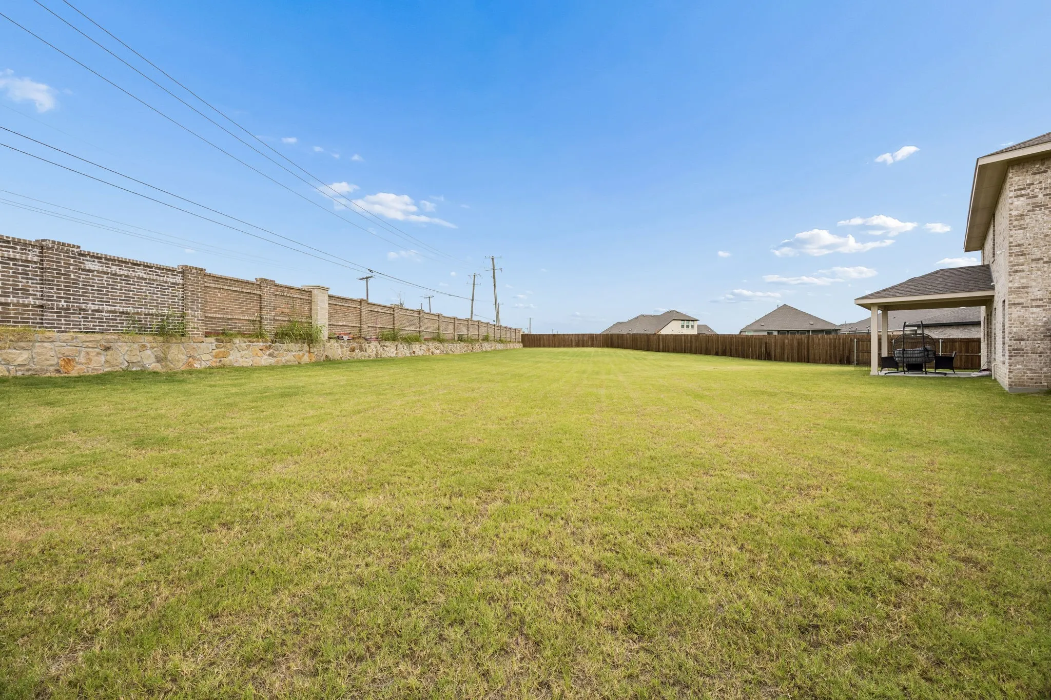 Expansive green space featuring a large brick privacy wall, a wood fence, and a covered patio area
