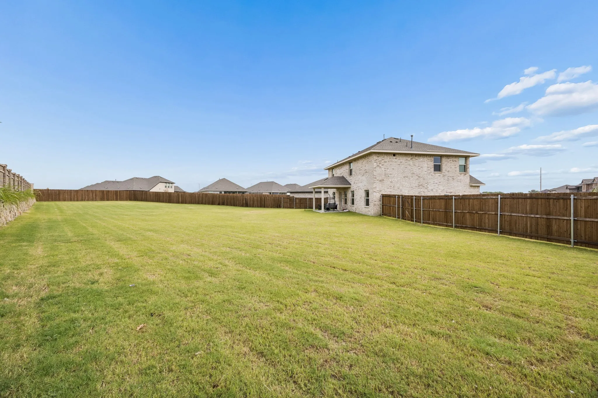 Expansive backyard featuring a large grass lawn, perimeter wood fencing, and a two-story residence with a covered patio